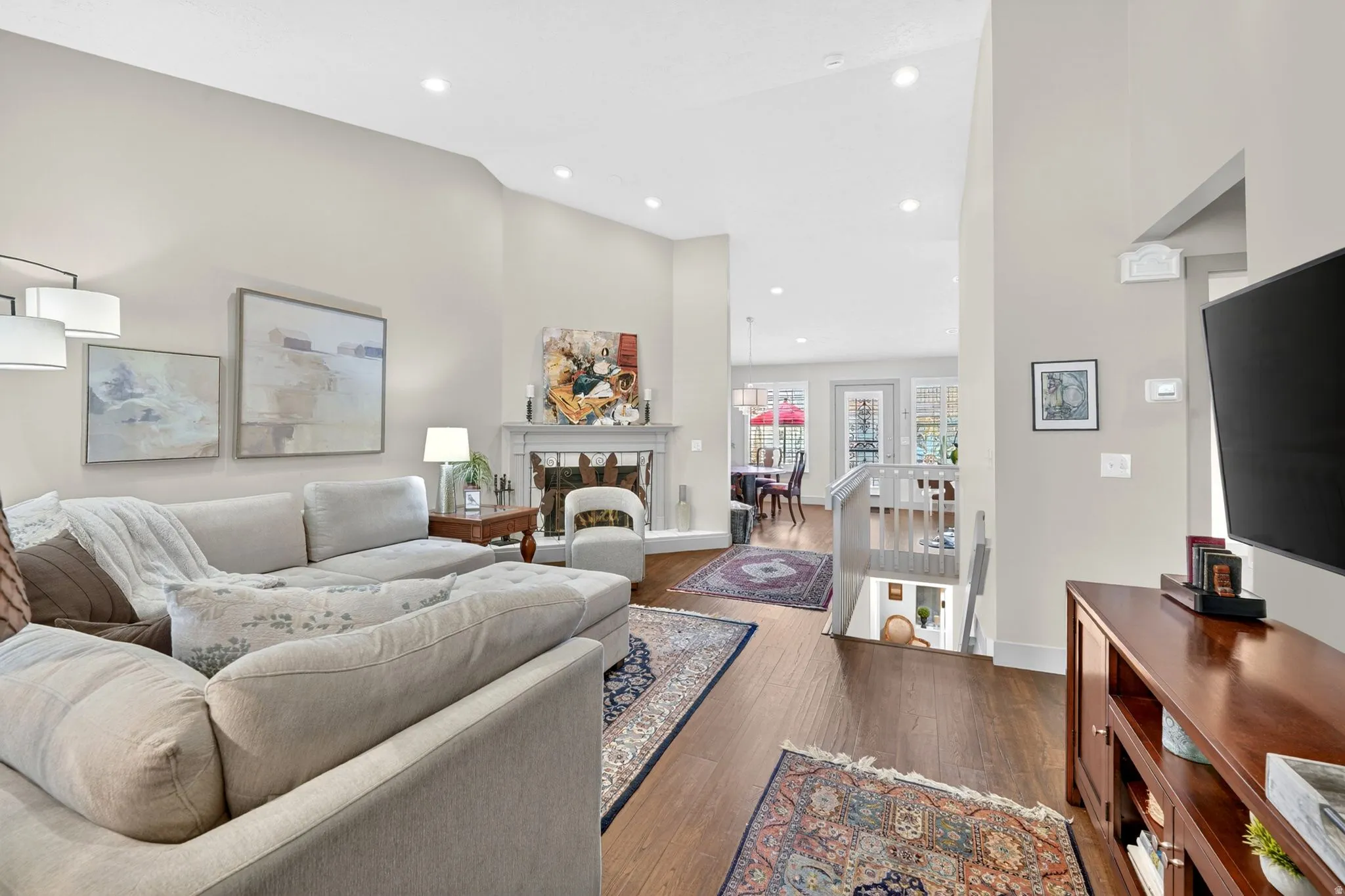 Living room with a fireplace with raised hearth, dark wood-style floors, vaulted ceiling, and recessed lighting