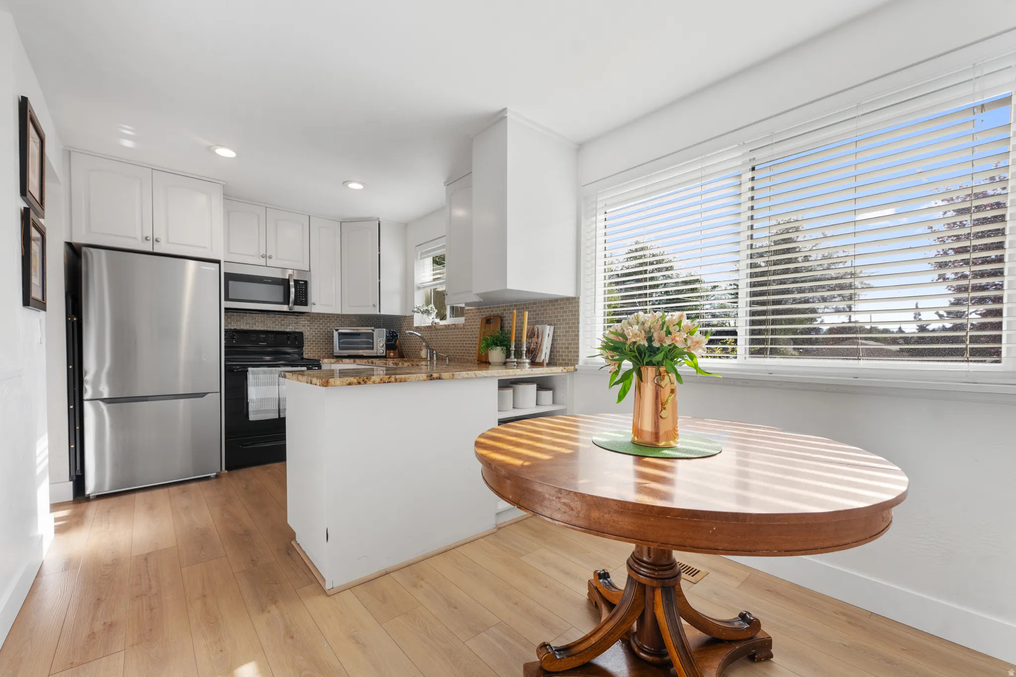 Kitchen featuring stainless steel appliances, light stone counters, white cabinets, a peninsula, and light wood finished floors