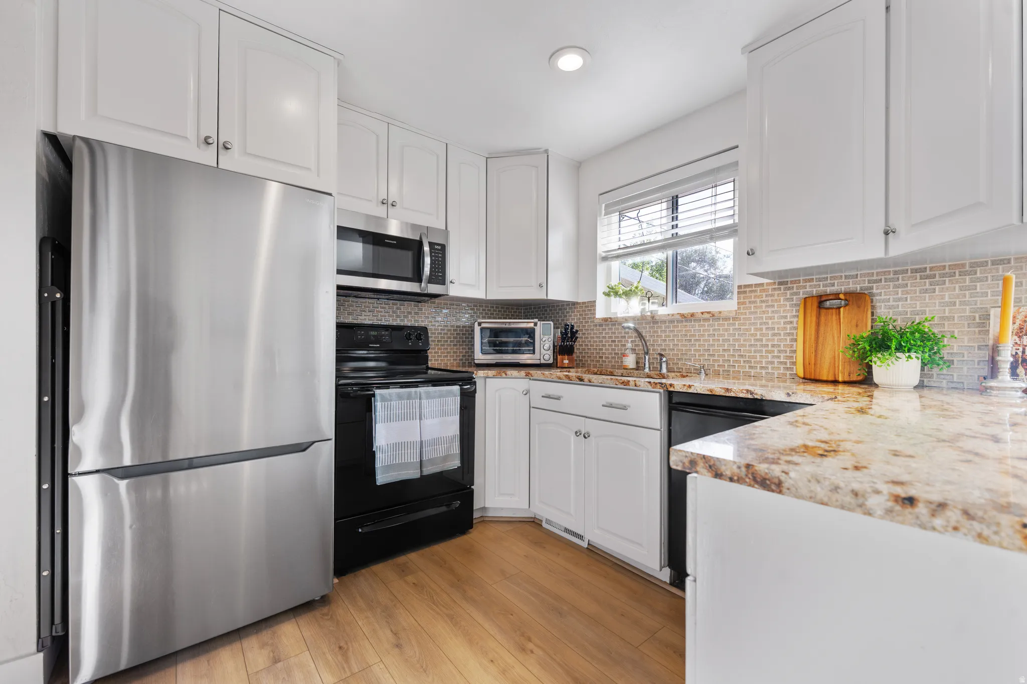 Kitchen featuring light stone countertops, black appliances, white cabinetry, light wood-style floors, and recessed lighting