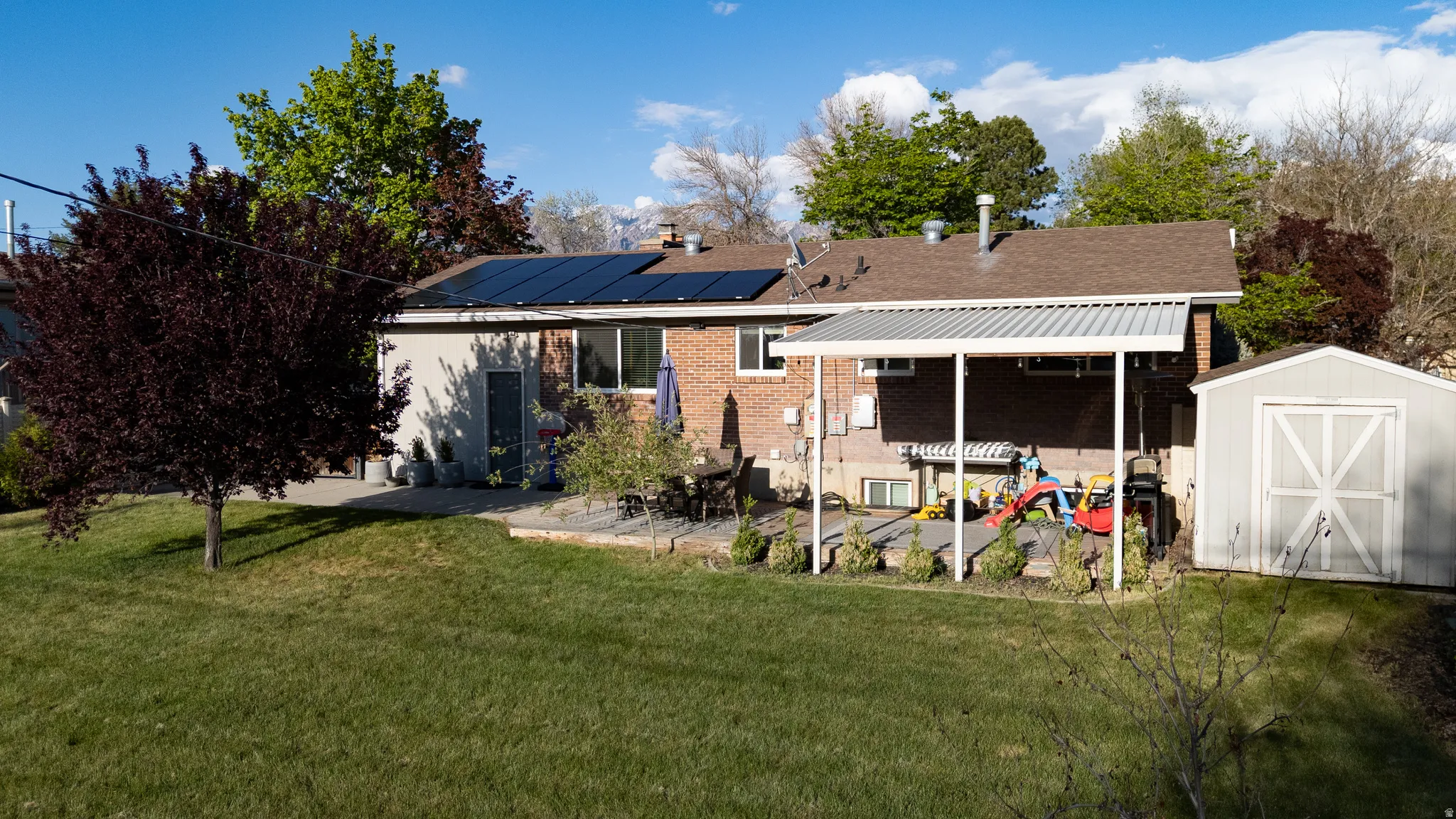 Back of property with a storage unit, a yard, a patio, solar panels, and brick siding