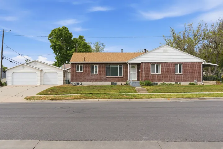 Ranch-style home featuring a detached garage, a front lawn, an outdoor structure, and brick siding