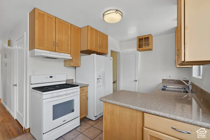 Kitchen with light wood-finish cabinetry, white appliances, and a double basin stainless steel sink