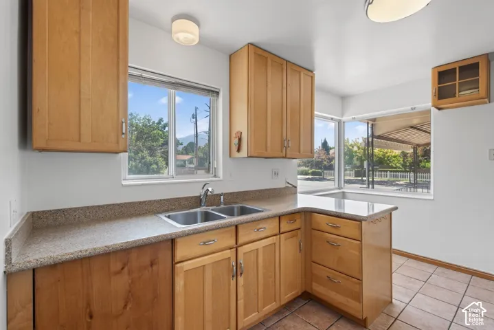 Kitchen featuring light wood cabinetry, a double basin stainless steel sink, speckled countertops, and tile flooring