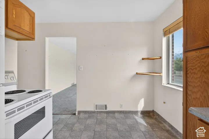 Kitchen featuring wood finish cabinetry, white electric range oven, dark carpet, open shelves, and stone finish flooring