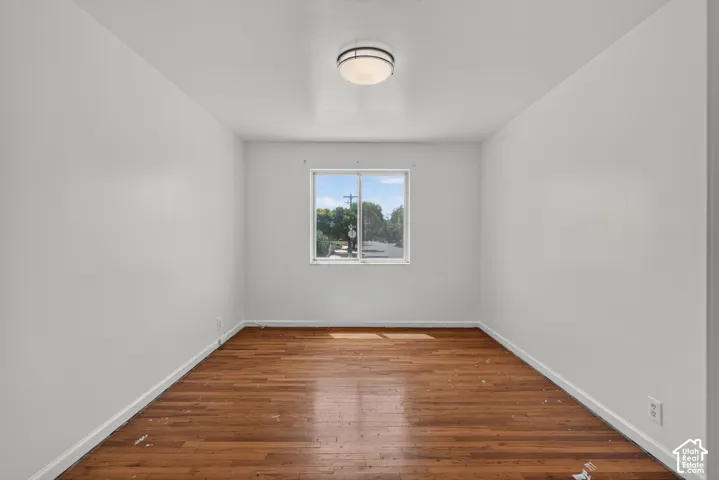 Interior room featuring wood-finish flooring, white painted walls, and a single window with exterior street views
