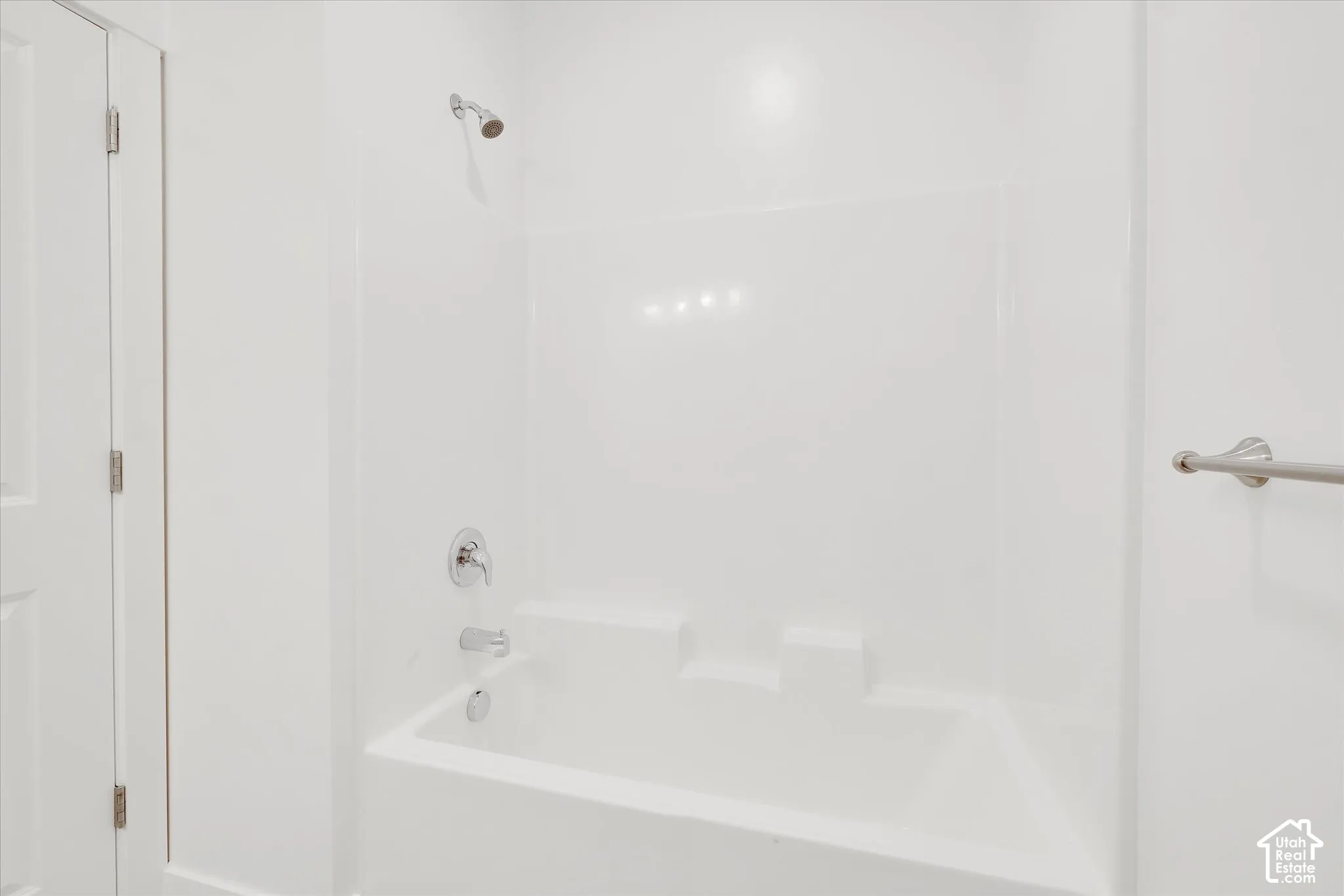 Tub and shower combination with white surround, chrome plumbing fixtures, and wall-mounted metal towel bar