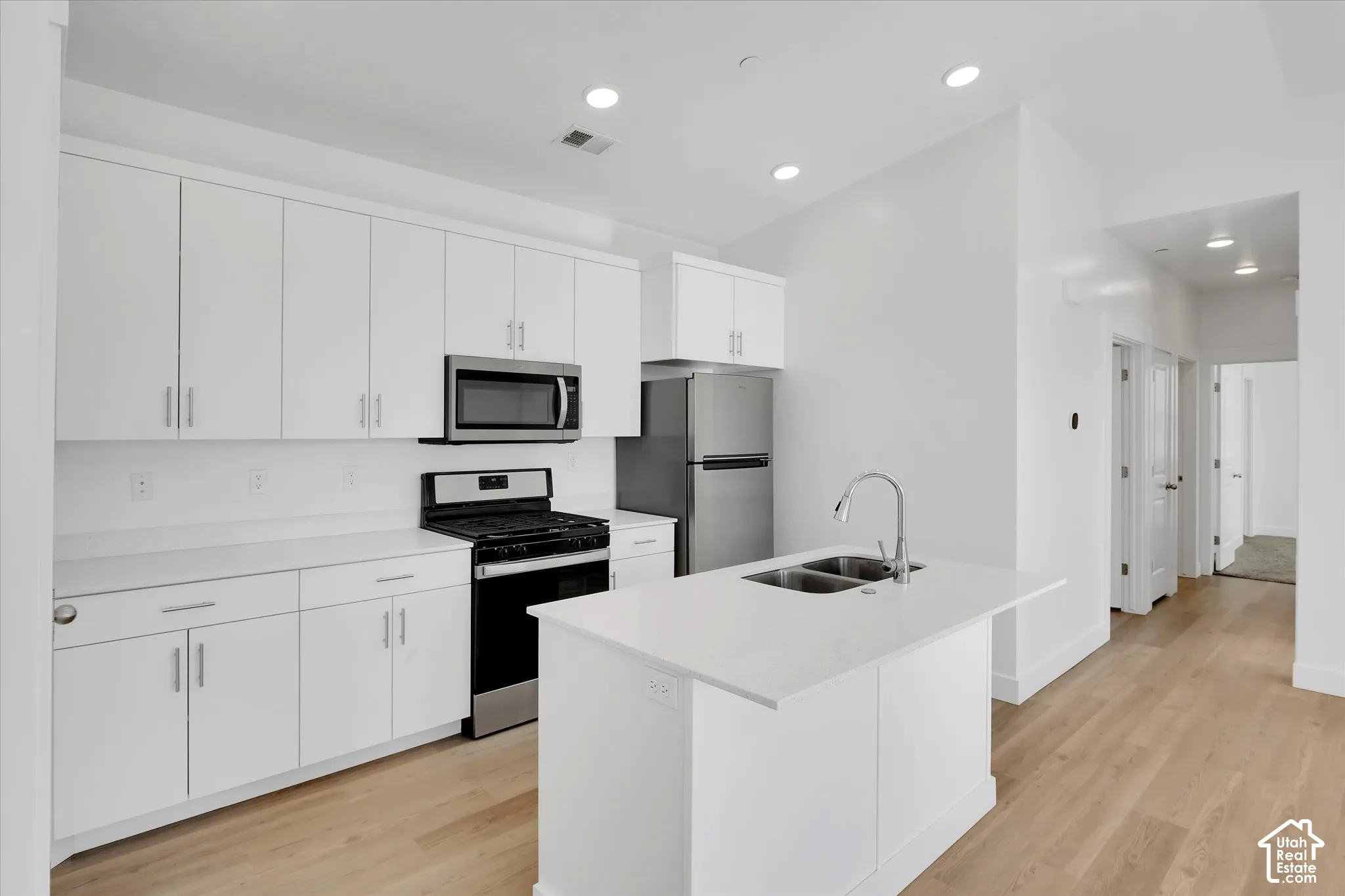 Kitchen featuring white cabinetry, solid surface countertops, a central island with a double-basin undermount sink, stainless steel appliances, and wood-finish flooring