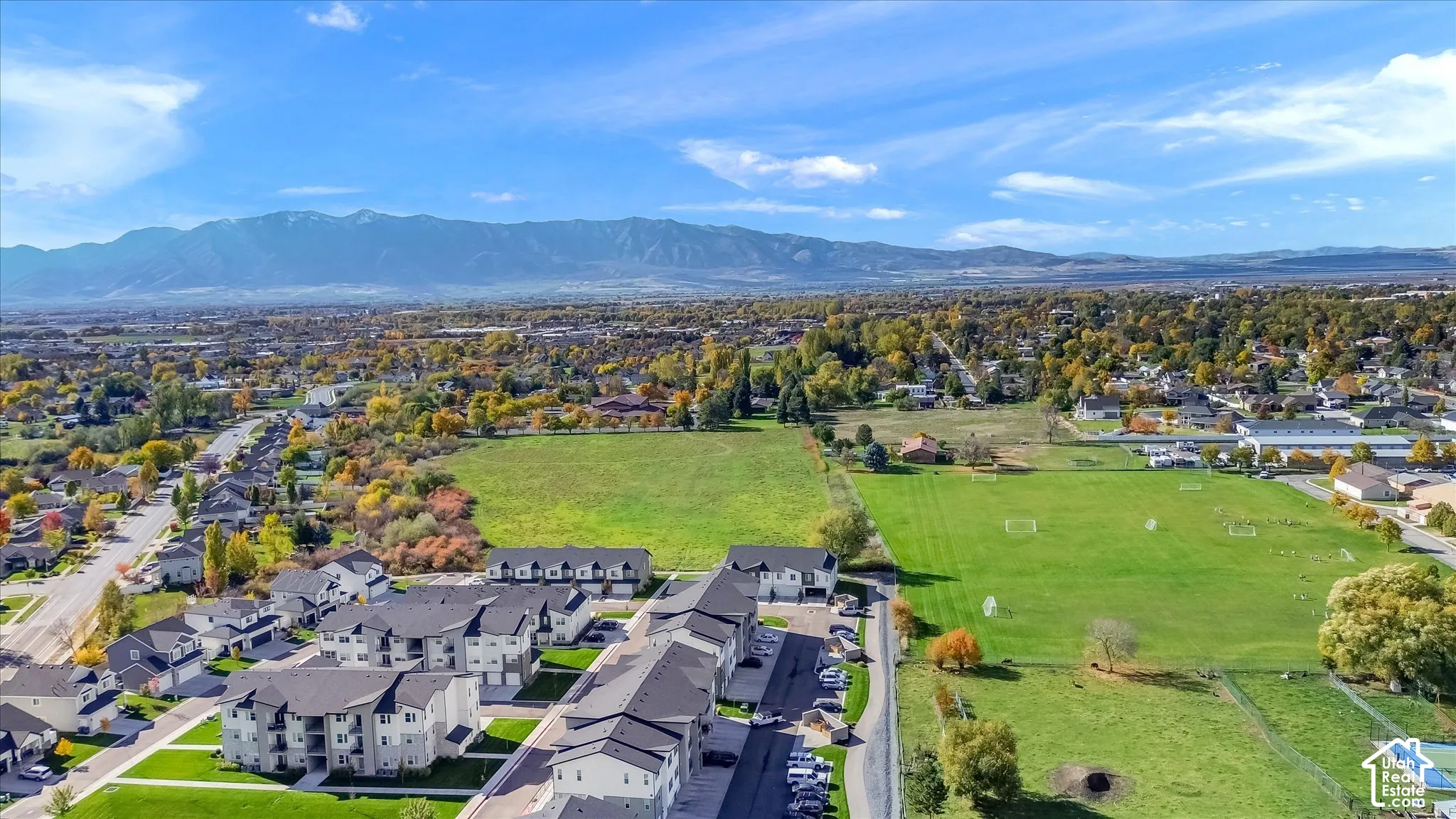 Aerial perspective featuring multi-story residential buildings, expansive open green space, and prominent mountain range backdrop