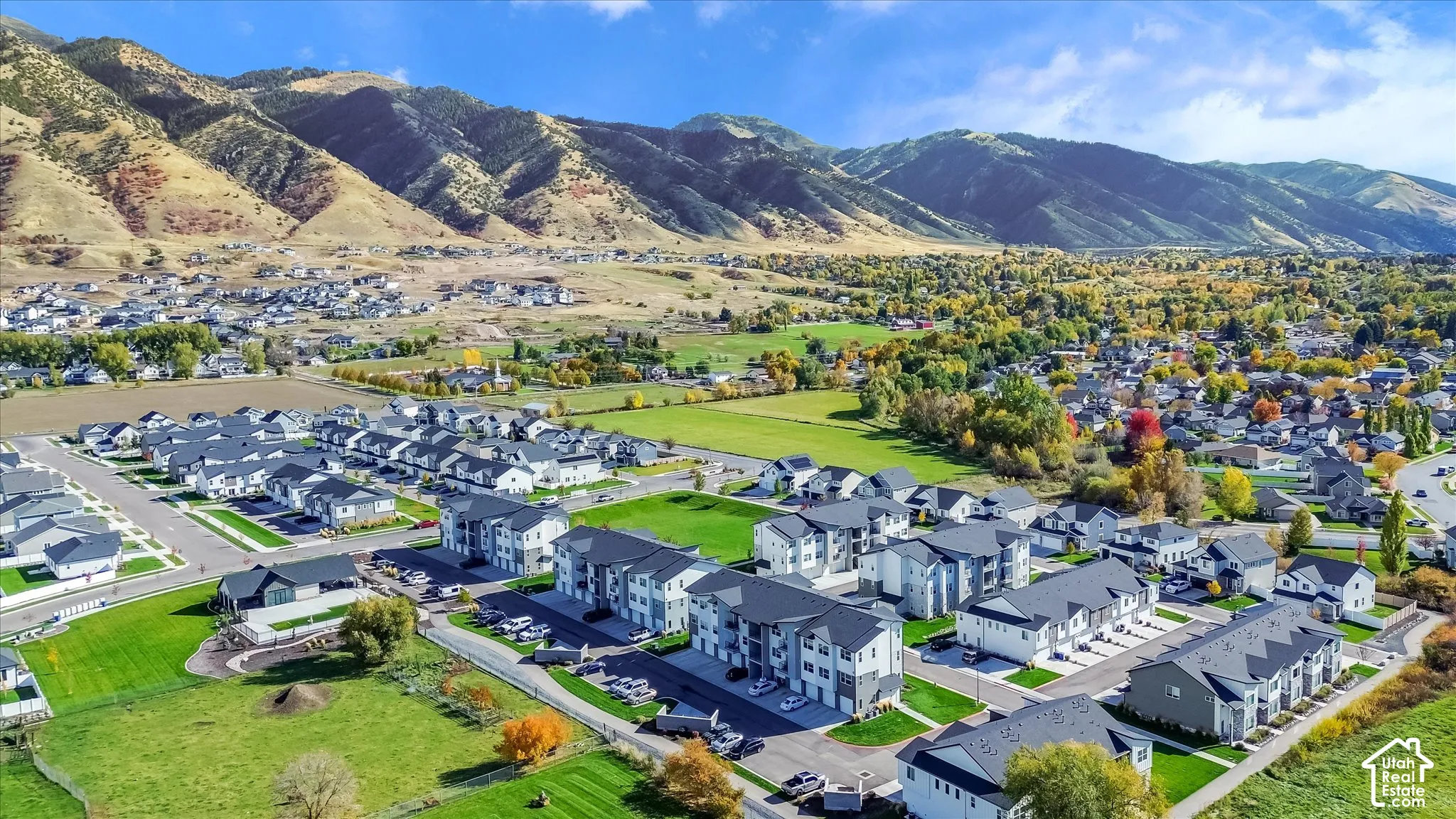 Aerial perspective featuring multi-story residential structures with dark-toned roofing, set against a backdrop of prominent mountain ranges and open green spaces