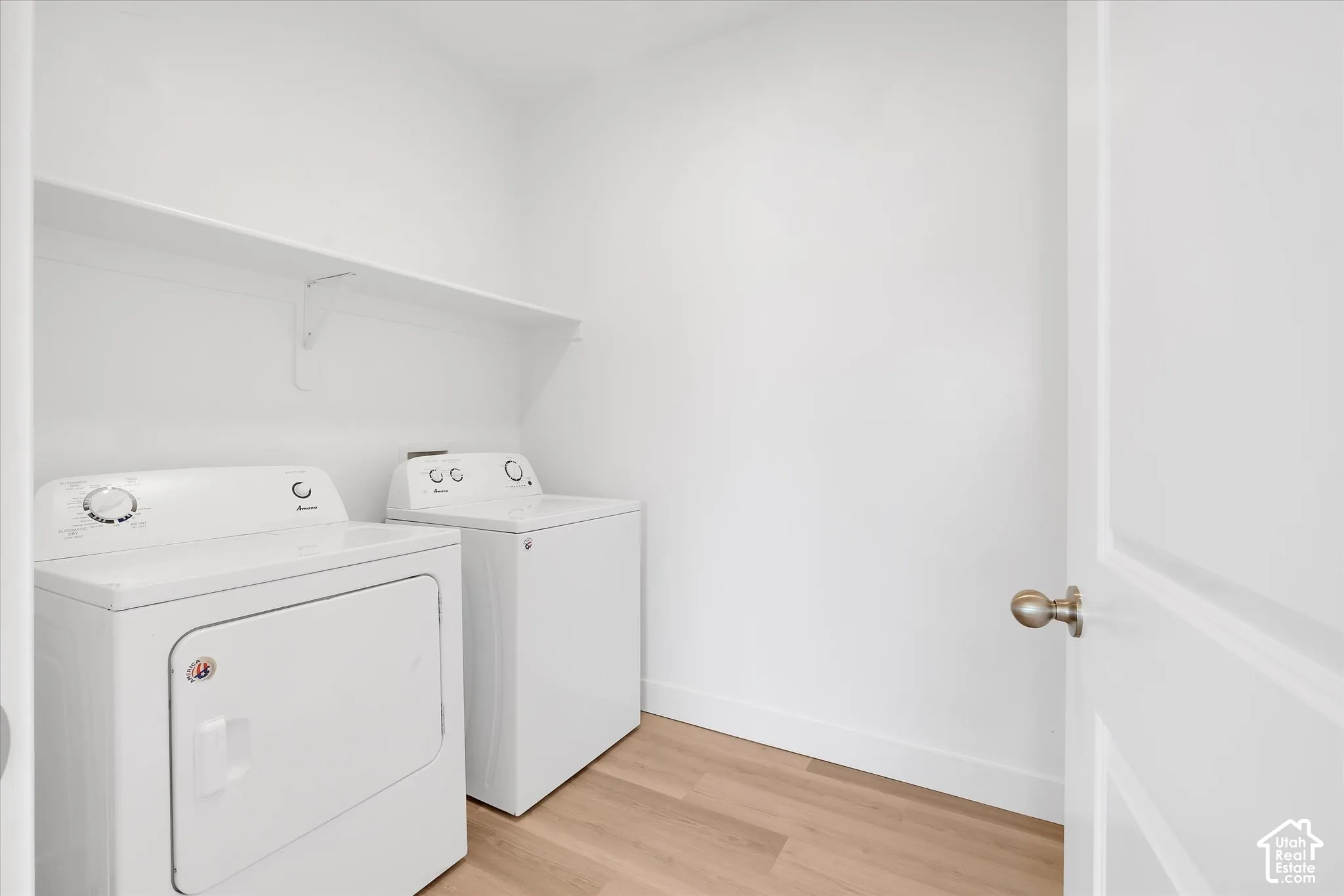 Utility room featuring wood-finish flooring, white walls, and a wall-mounted storage shelf