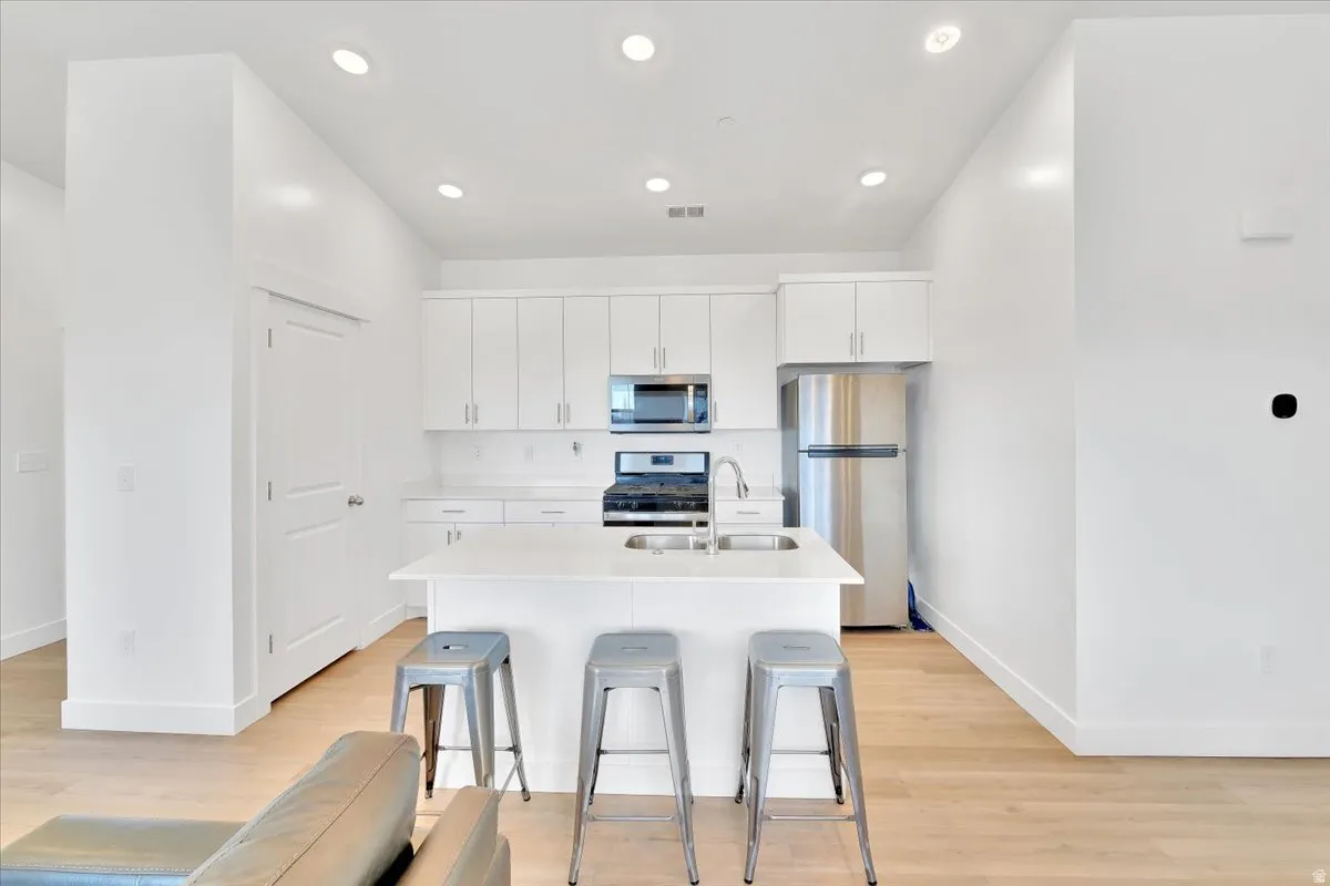 Kitchen featuring stainless steel appliances, white cabinets, light wood-style floors, an island with sink, and recessed lighting