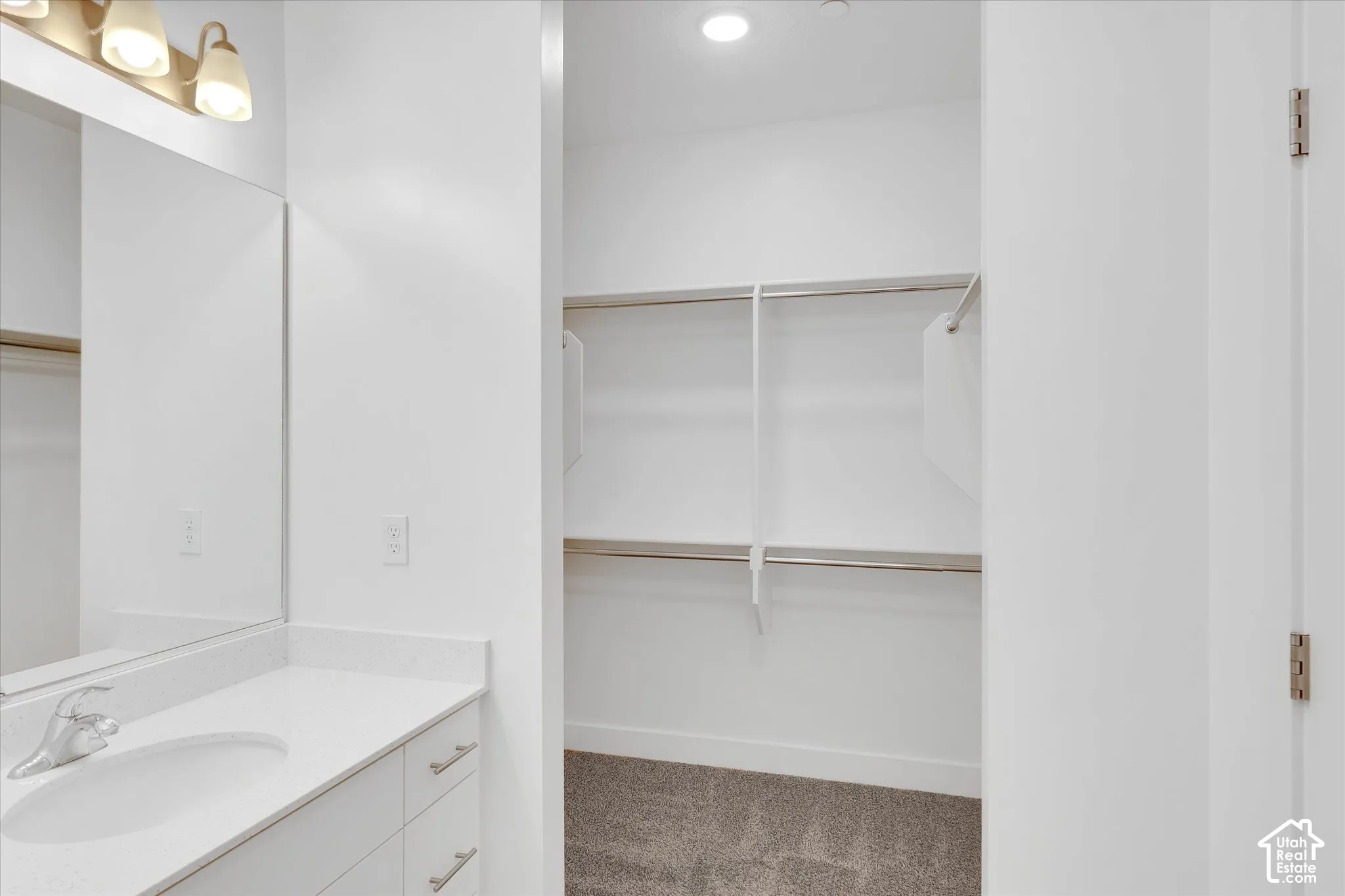 Vanity featuring a solid surface countertop, integrated sink, and polished hardware, accompanied by a walk-in closet with built-in metal shelving