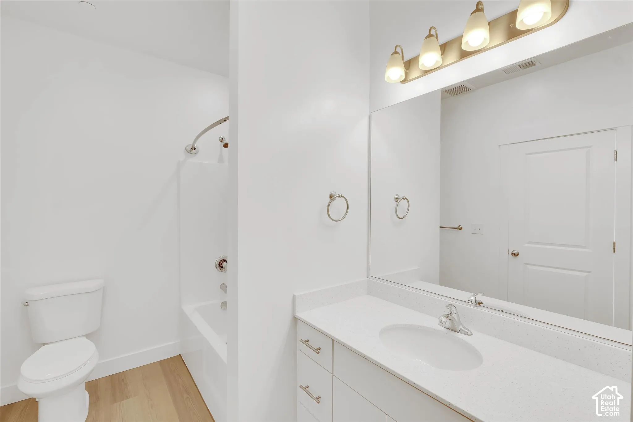 Bathroom featuring wood-finish flooring, a white vanity with a composite countertop, a full-width mirror, a multi-bulb vanity light fixture, and a tub-shower combination