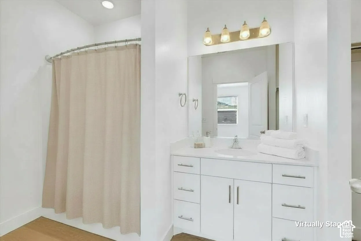 Bathroom featuring a white vanity with integrated basin, polished metal hardware, large wall-mounted mirror, four-light vanity fixture, and a curved shower rod