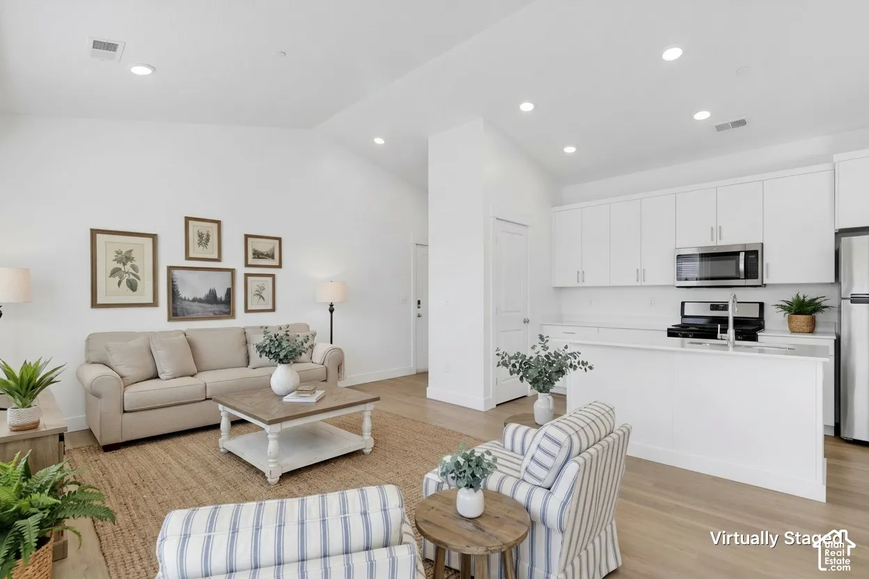 Open floor plan featuring vaulted ceilings, recessed lighting, white cabinetry, a kitchen island, and wood-finish flooring