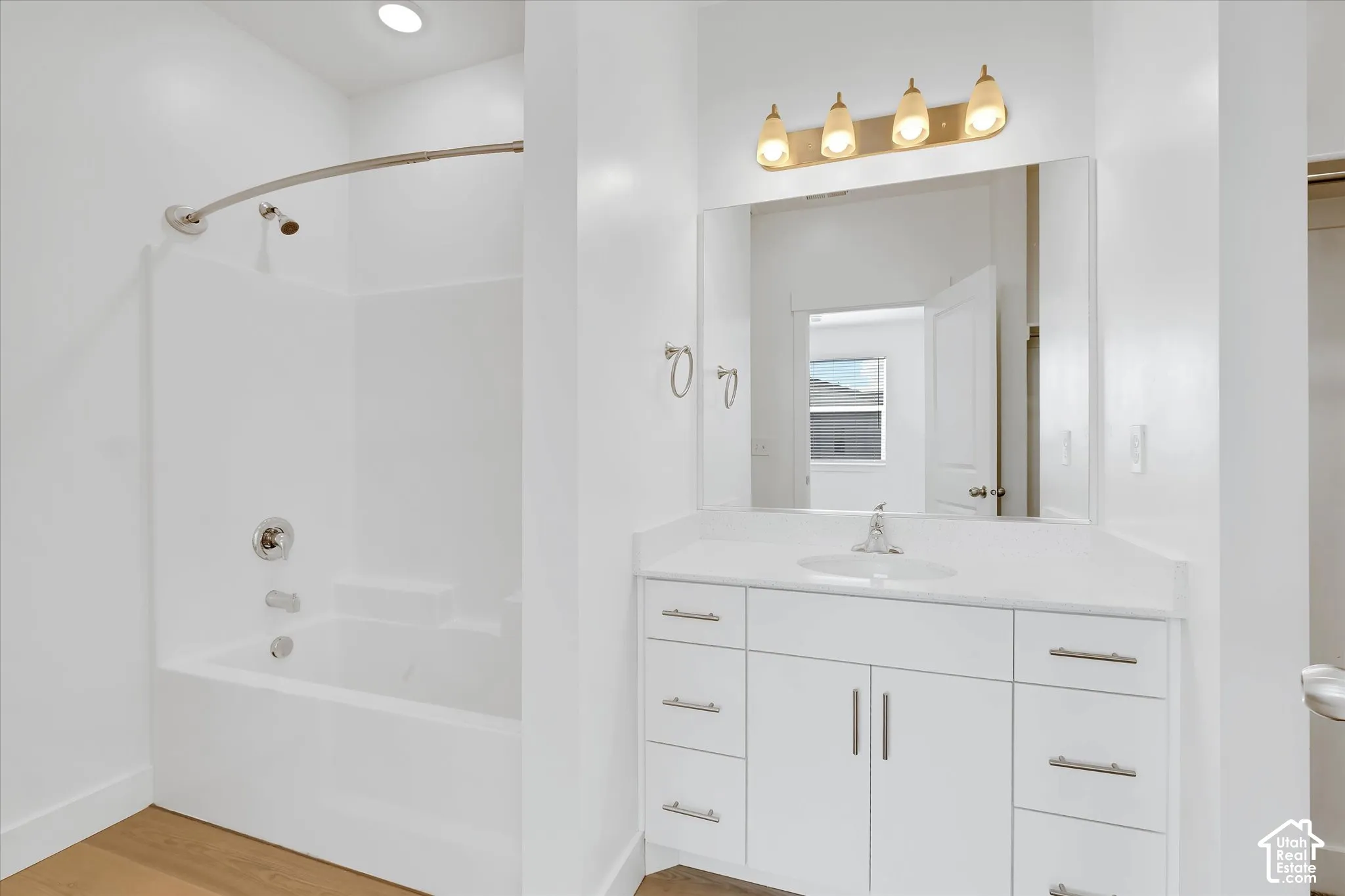 Bathroom featuring a vanity with white cabinetry, a solid-surface countertop, an integrated sink, a full-width mirror, and a tub-shower combination with a curved shower rod