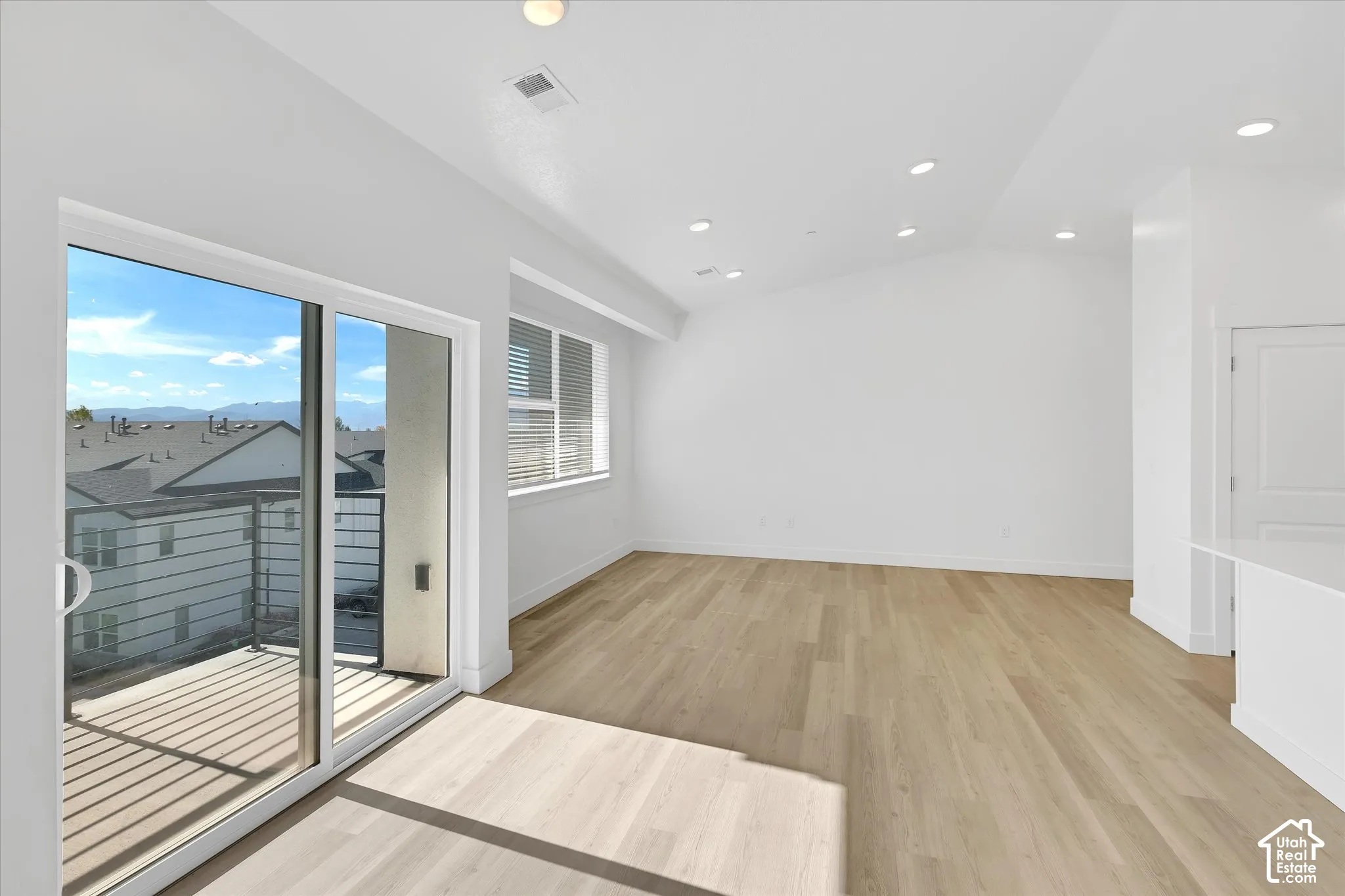 Vaulted ceilings, wood-finish flooring, recessed lighting, and a glass sliding door opening to a private balcony