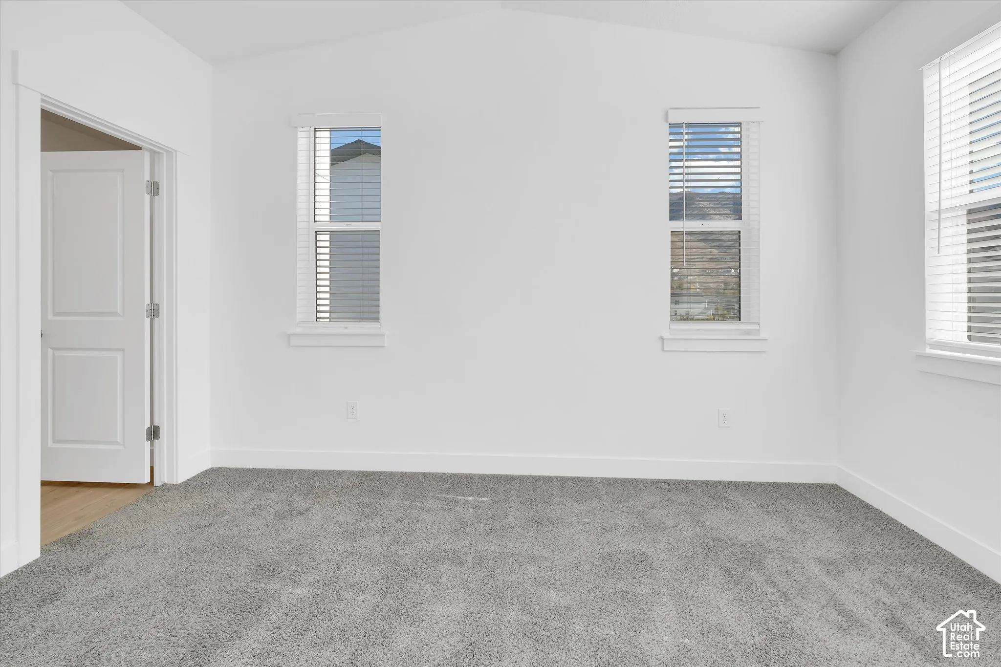 Primary Suite, Vaulted ceilings, neutral carpeting, and three windows featuring white trim and blinds