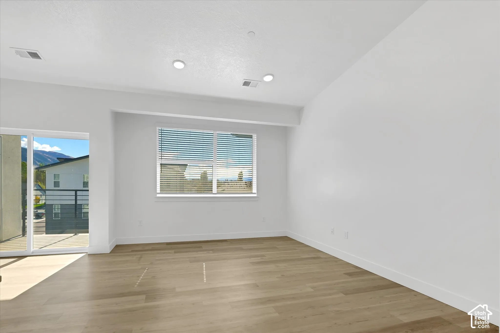 Vaulted ceilings, wood-finish flooring, recessed lighting, and sliding glass door access to an exterior balcony
