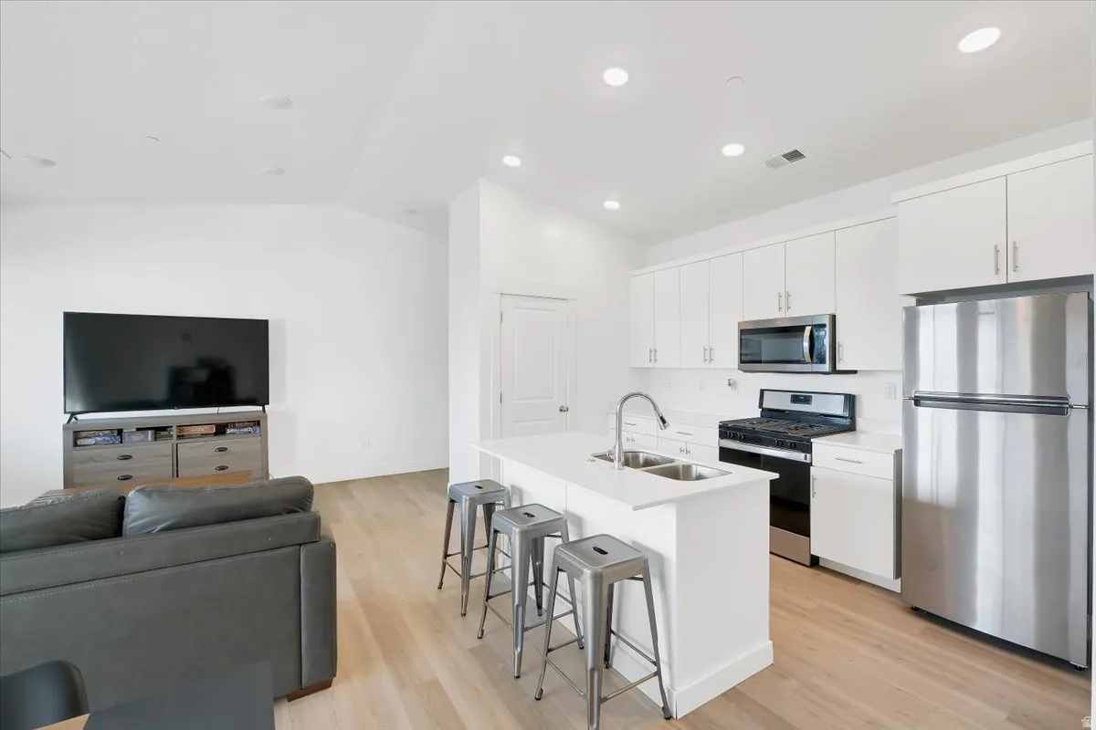 Kitchen featuring stainless steel appliances, open floor plan, light wood finished floors, a breakfast bar area, and white cabinets