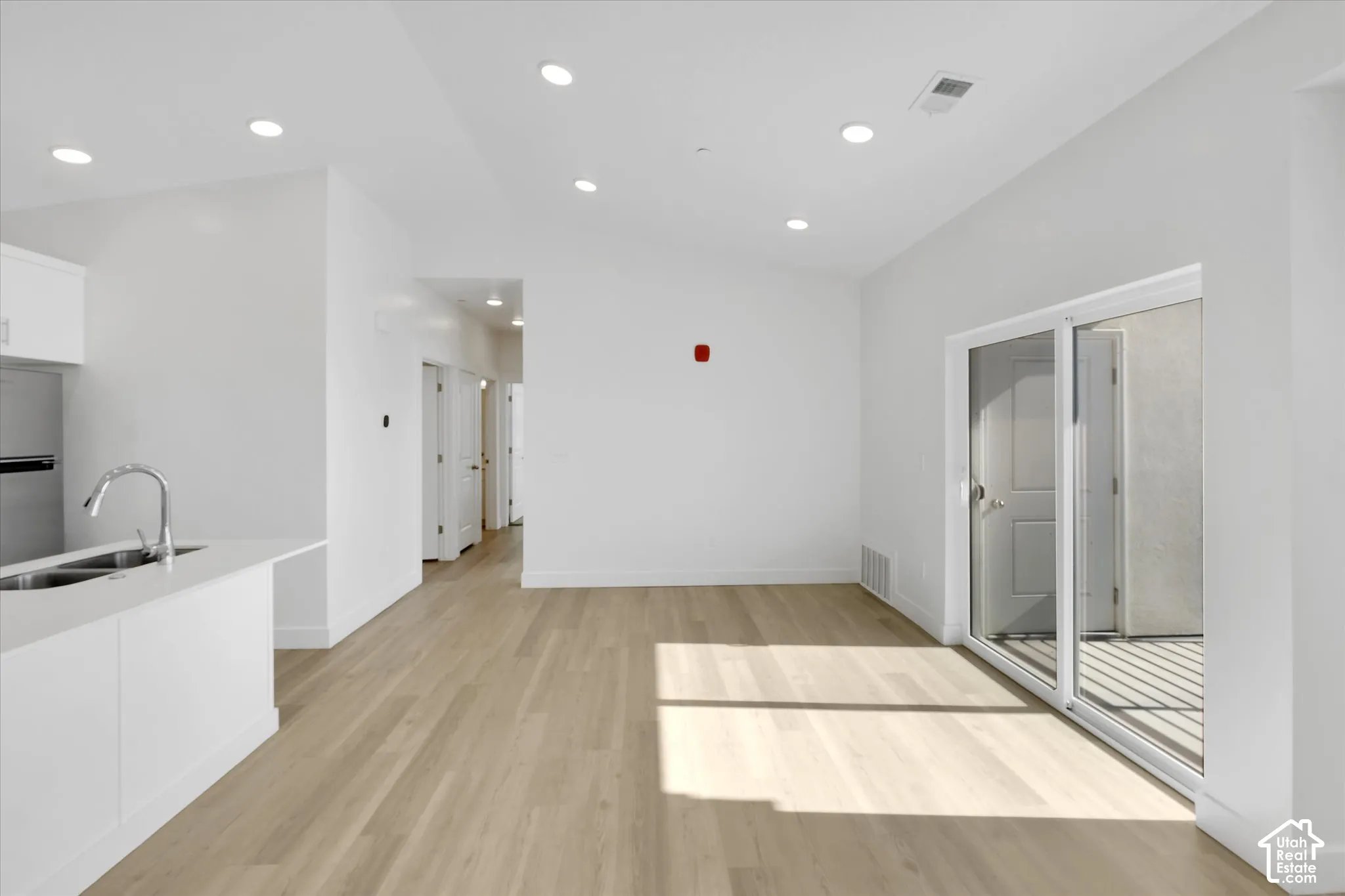 Open-concept interior featuring vaulted ceilings, recessed lighting, wood-finish flooring, and sliding glass doors leading to an exterior space