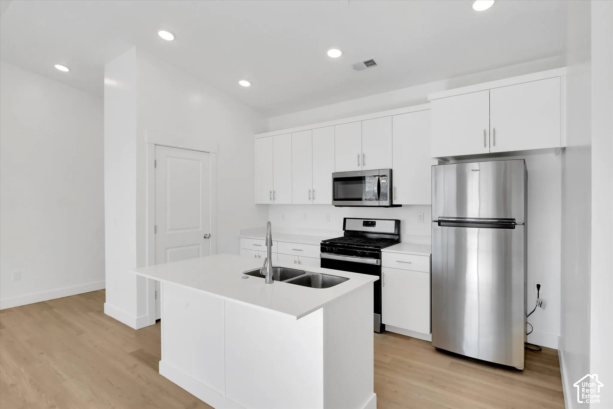 Kitchen featuring white shaker-style cabinetry, quartz countertops, a center island with a dual-basin undermount sink, stainless steel appliances, and wood-finish flooring