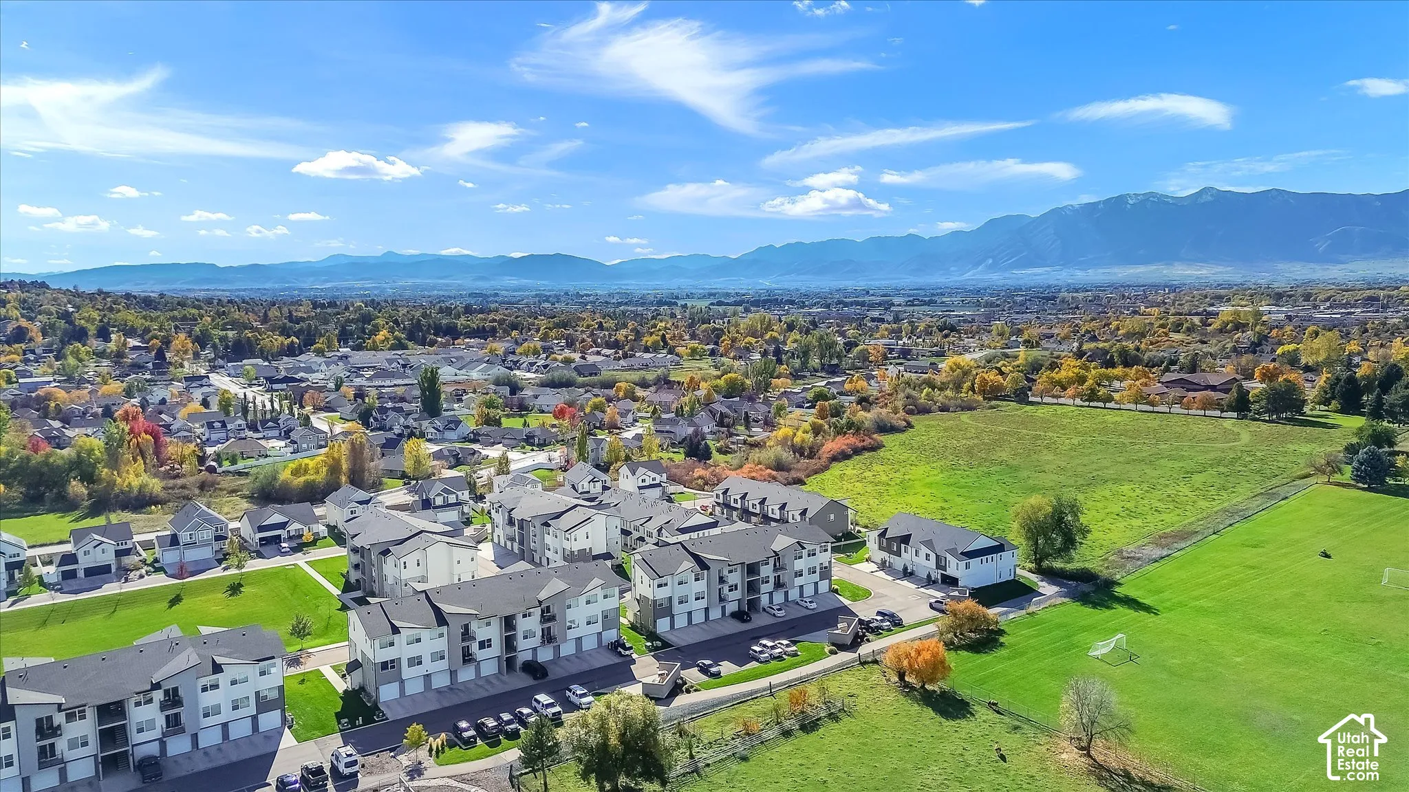 Aerial perspective featuring multi-story residential buildings with attached garages, surrounded by expansive green space and mountain backdrops