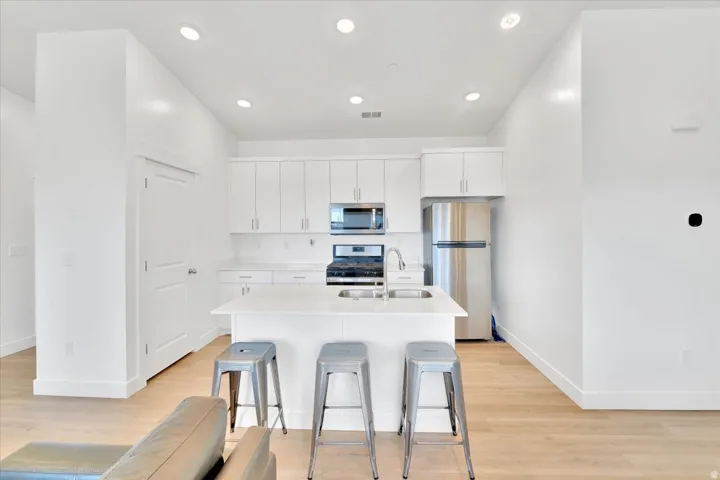 Kitchen featuring stainless steel appliances, white cabinets, light wood-style floors, an island with sink, and recessed lighting
