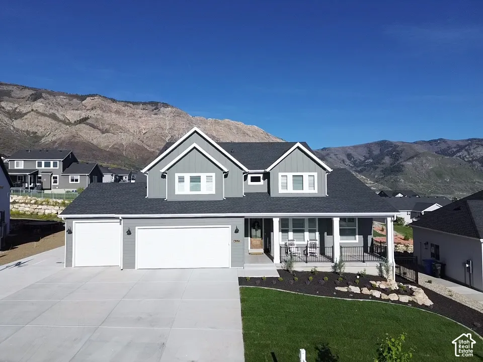 Two-story exterior with vertical siding, gable roofline, attached three-car garage, covered front porch with iron railing, and mountain backdrop