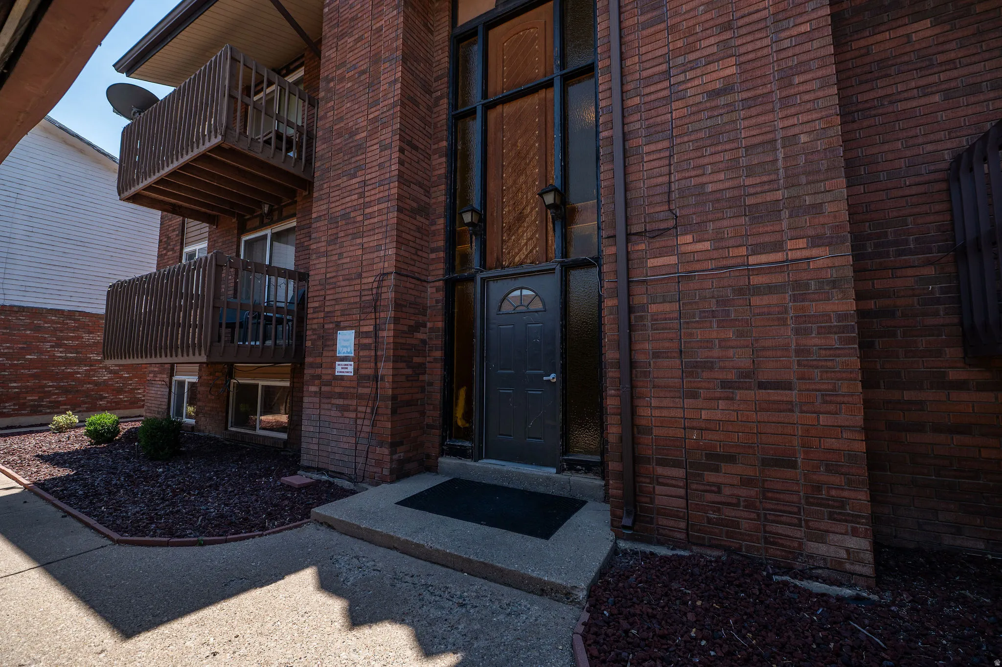 Brick facade building featuring a prominent glass-paneled entry door with an arched window detail and flanking wall-mounted light fixtures