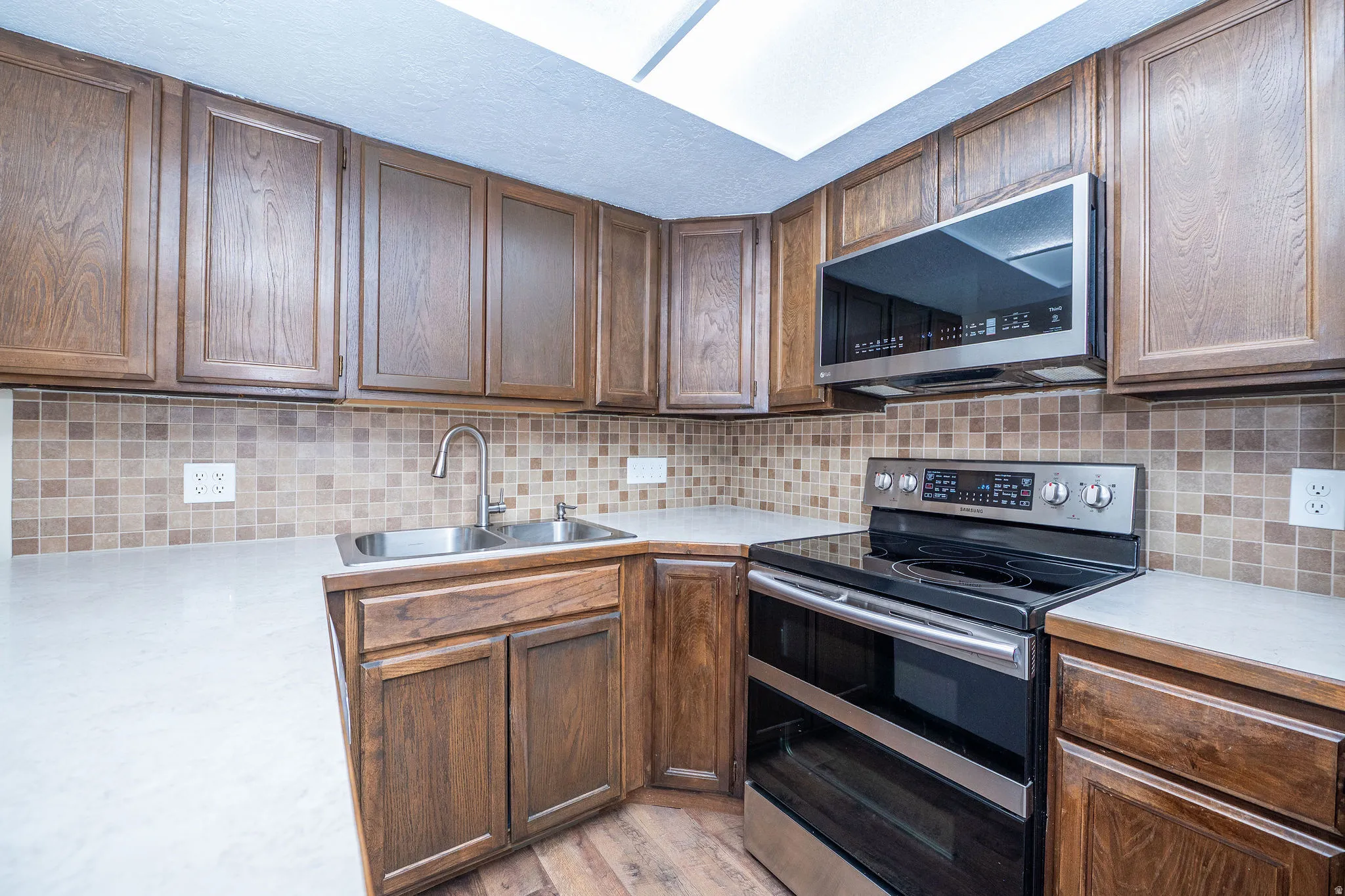 Kitchen featuring wood cabinetry, light countertops, a mosaic tile backsplash, stainless steel appliances, and wood-finish flooring