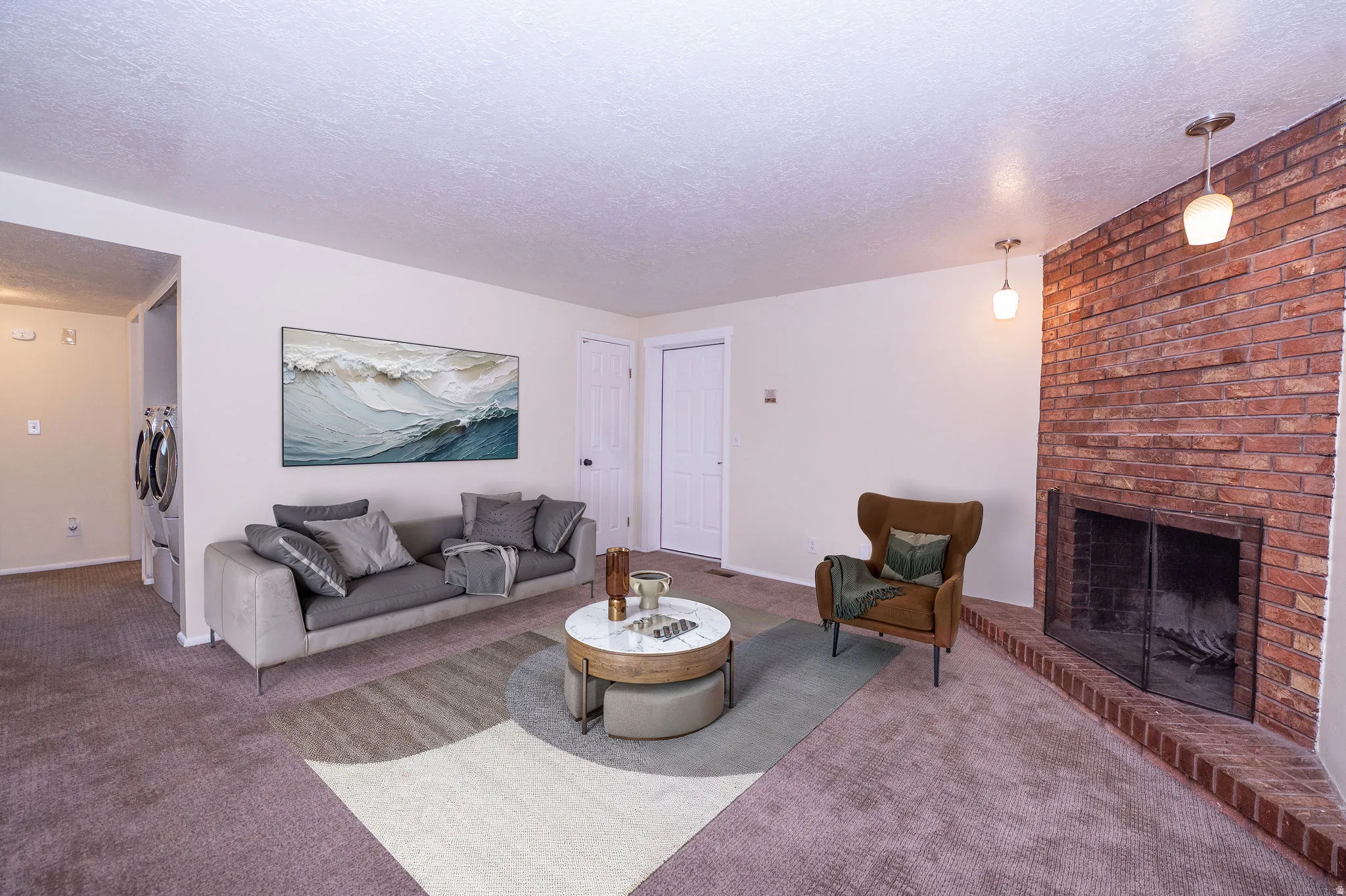 Living area featuring a brick fireplace with a raised hearth, recessed screen, and dual pendant lighting fixtures