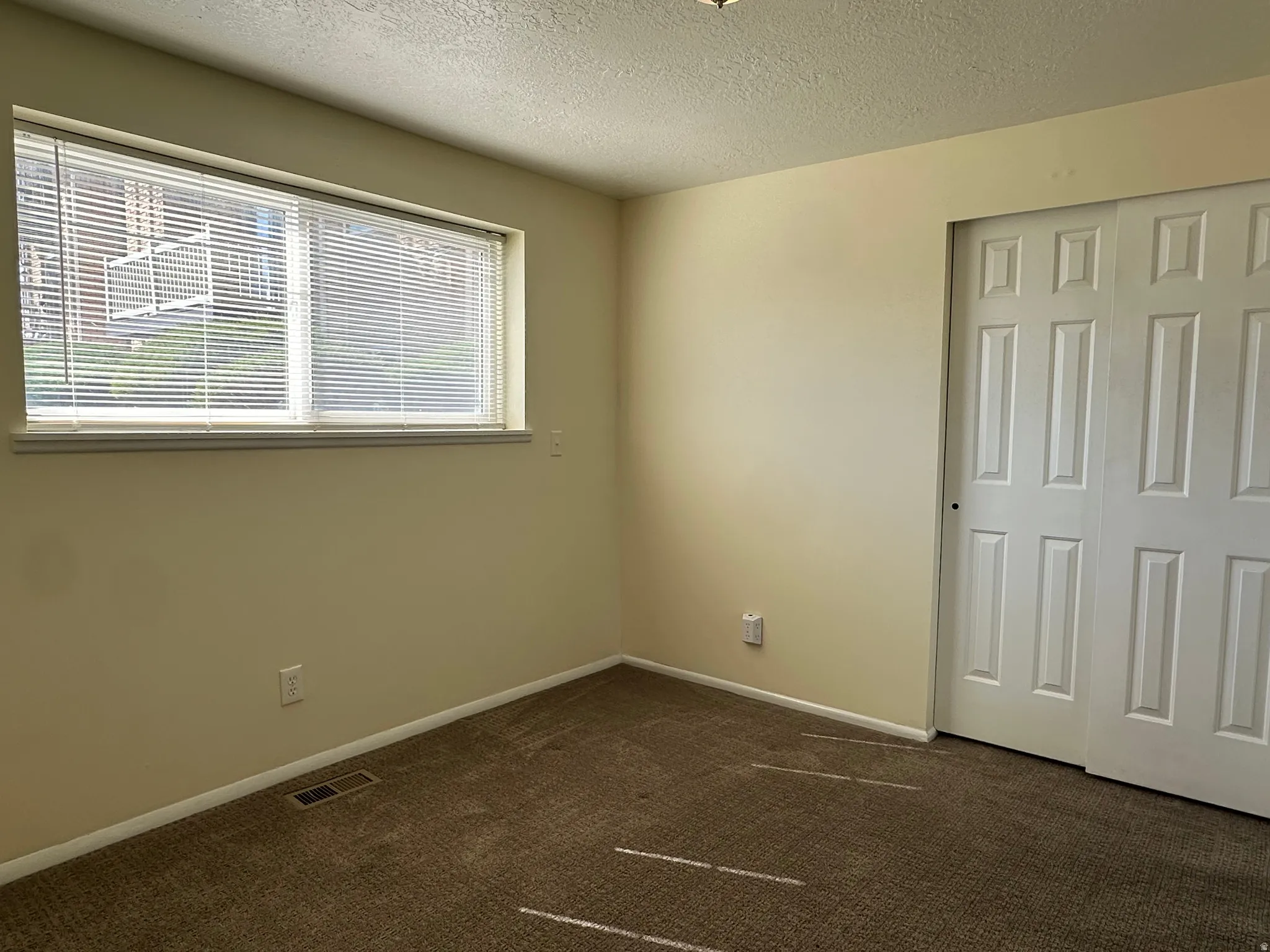 Unfurnished bedroom with dark colored carpet, a textured ceiling, and a closet