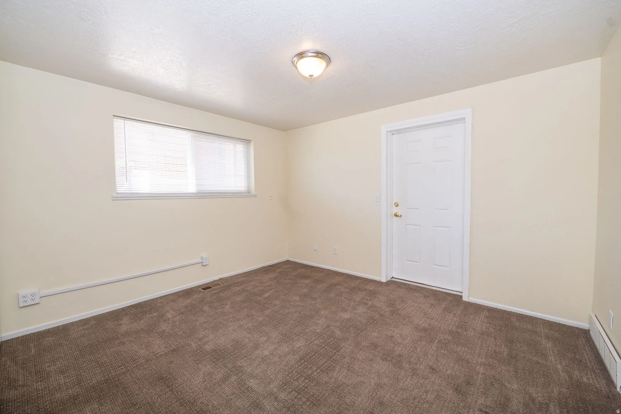 Neutral tone wall paint, brown carpeting, a window with blinds, a white paneled door, and a flush mount ceiling light fixture