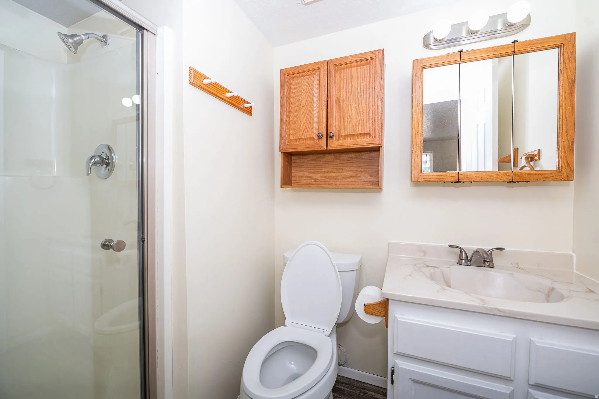 Bathroom featuring a glass-enclosed shower, white vanity with integrated sink, wood-finish medicine cabinet, wood-finish wall cabinet, and wood-look flooring