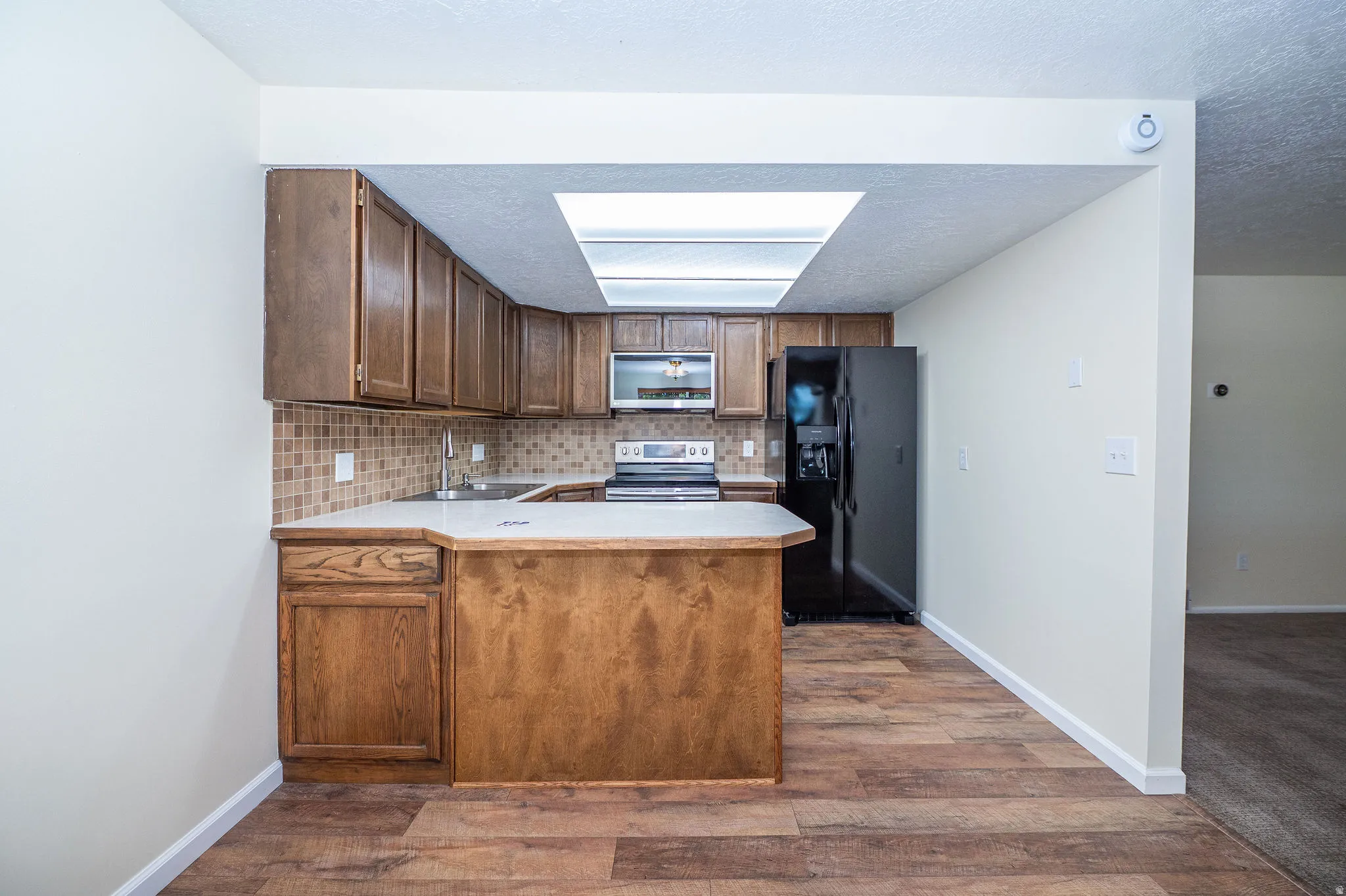 Kitchen featuring wood-finish flooring, wood cabinetry, a tiled backsplash, and a skylight