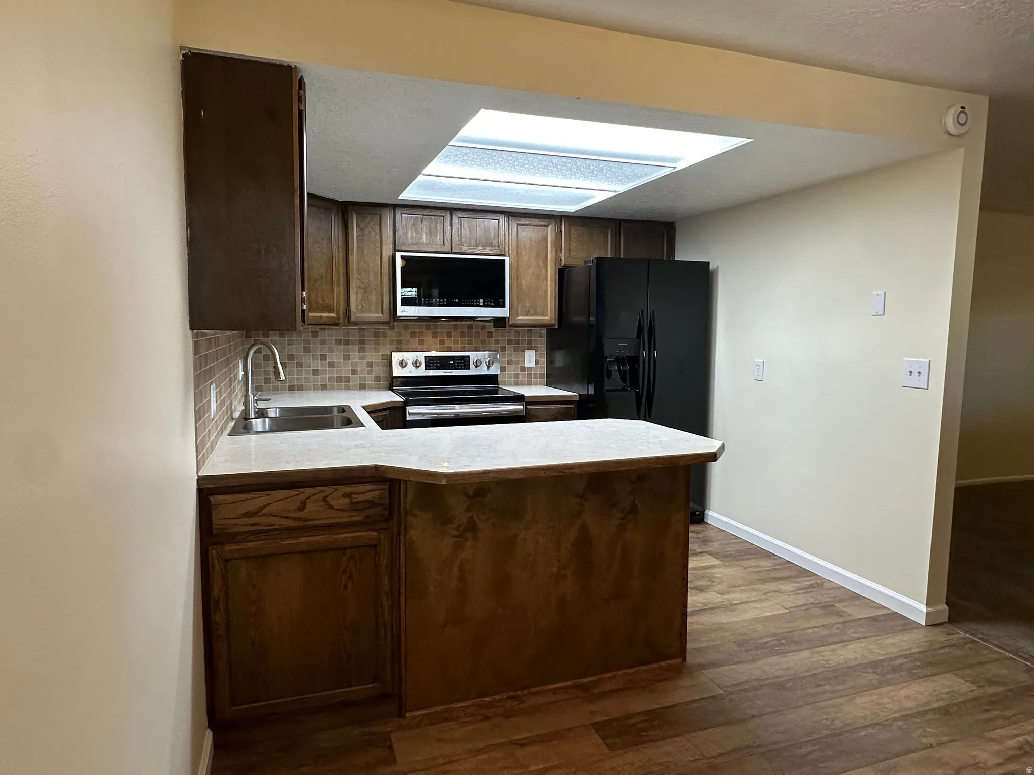 Kitchen with light countertops, black fridge, stainless steel electric range oven, a peninsula, and dark wood-style flooring