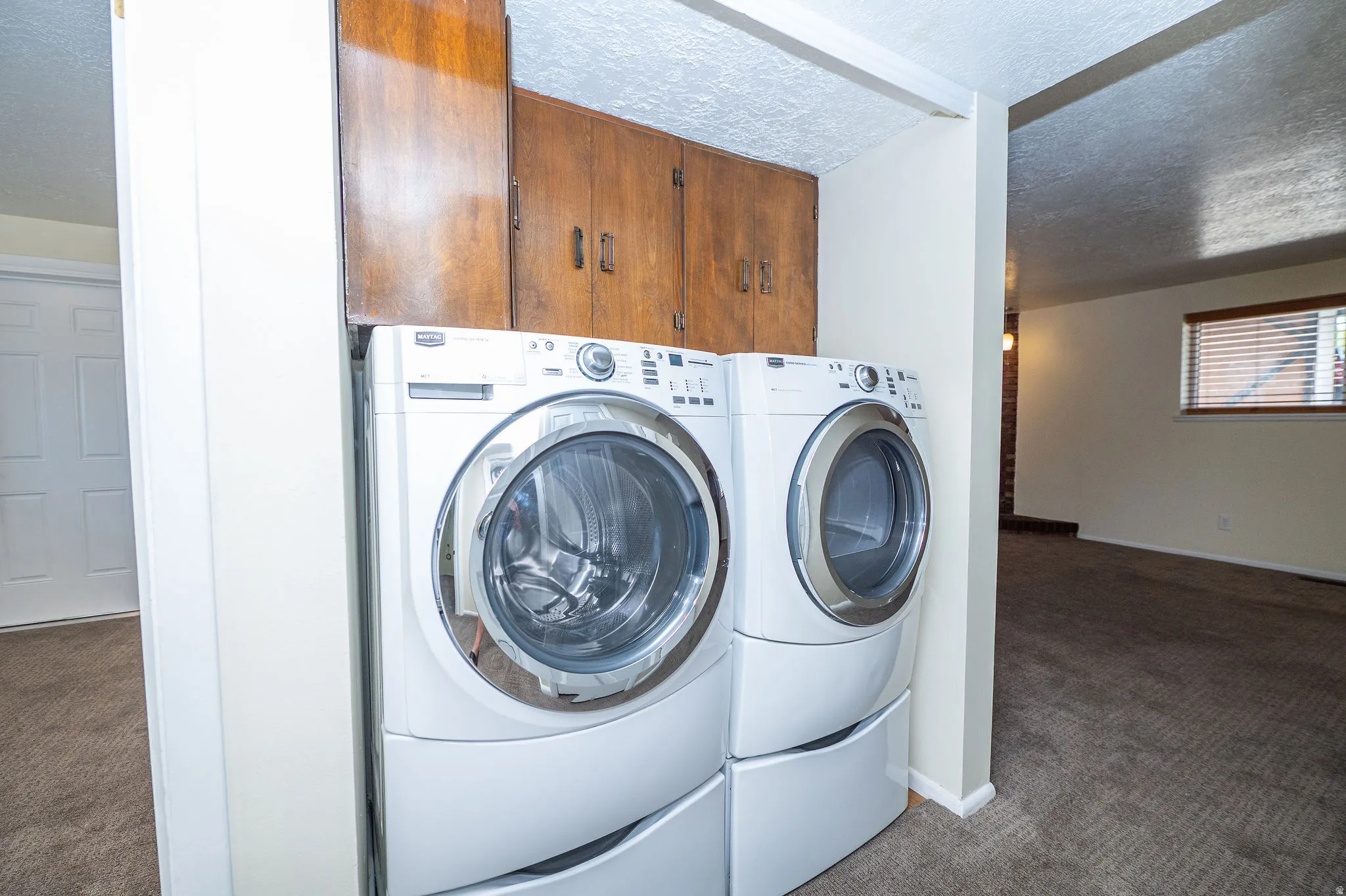 Dedicated laundry area featuring front-loading washer and dryer, wood-finish cabinetry, and neutral wall tones