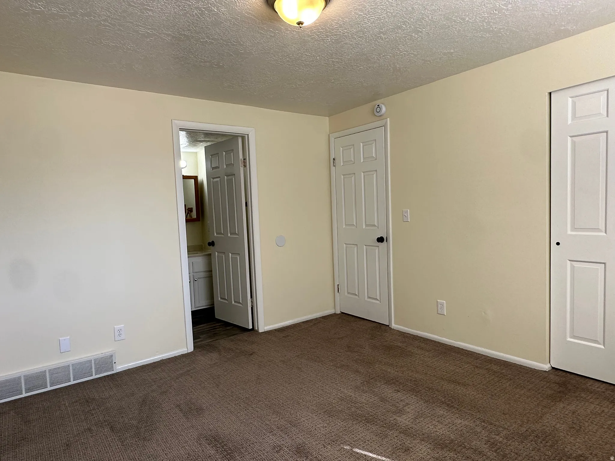 Unfurnished bedroom featuring dark carpet, a textured ceiling, and connected bathroom