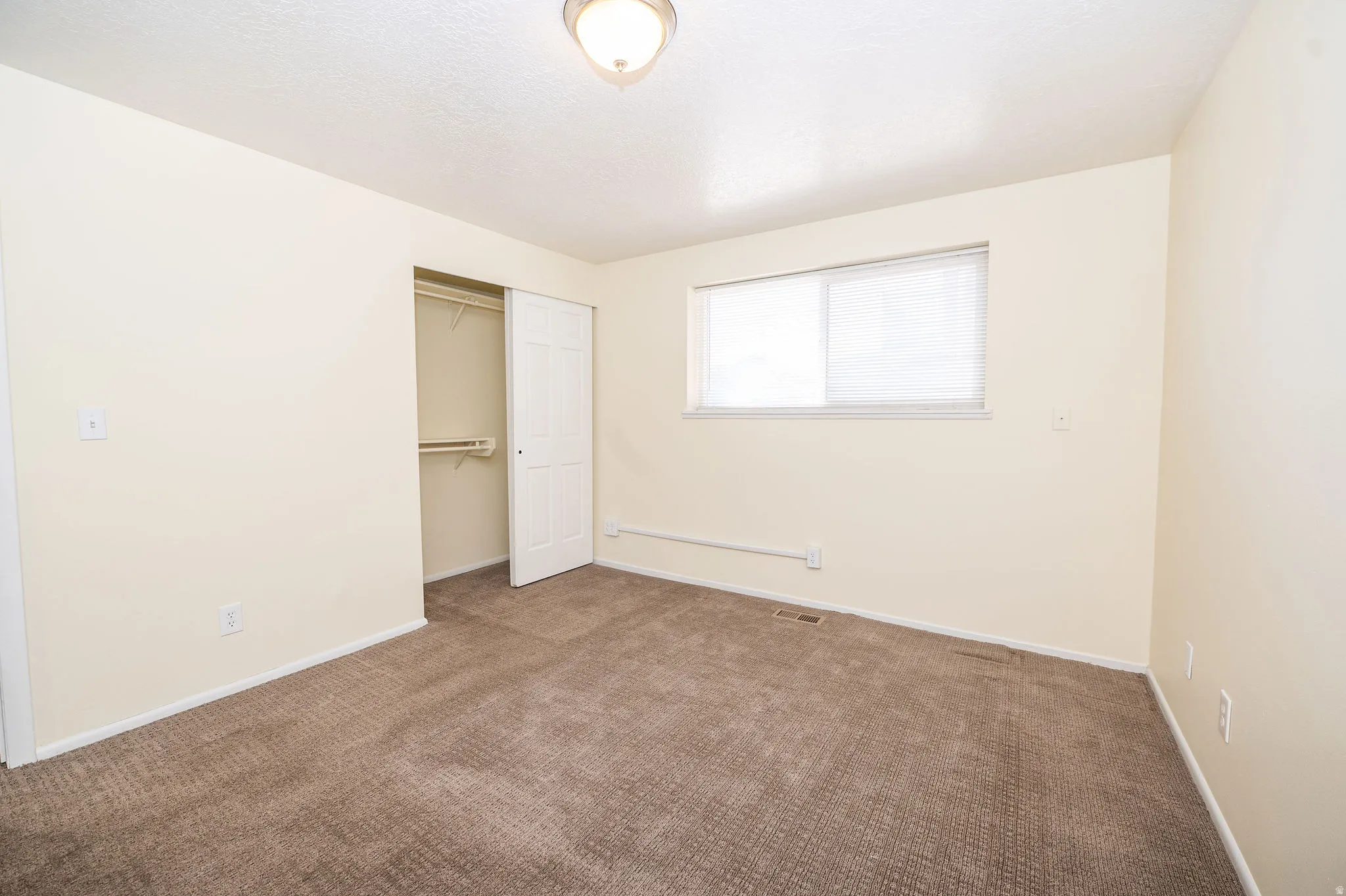Carpeted room featuring a double-door closet with shelving, a window with blinds, and neutral-toned walls