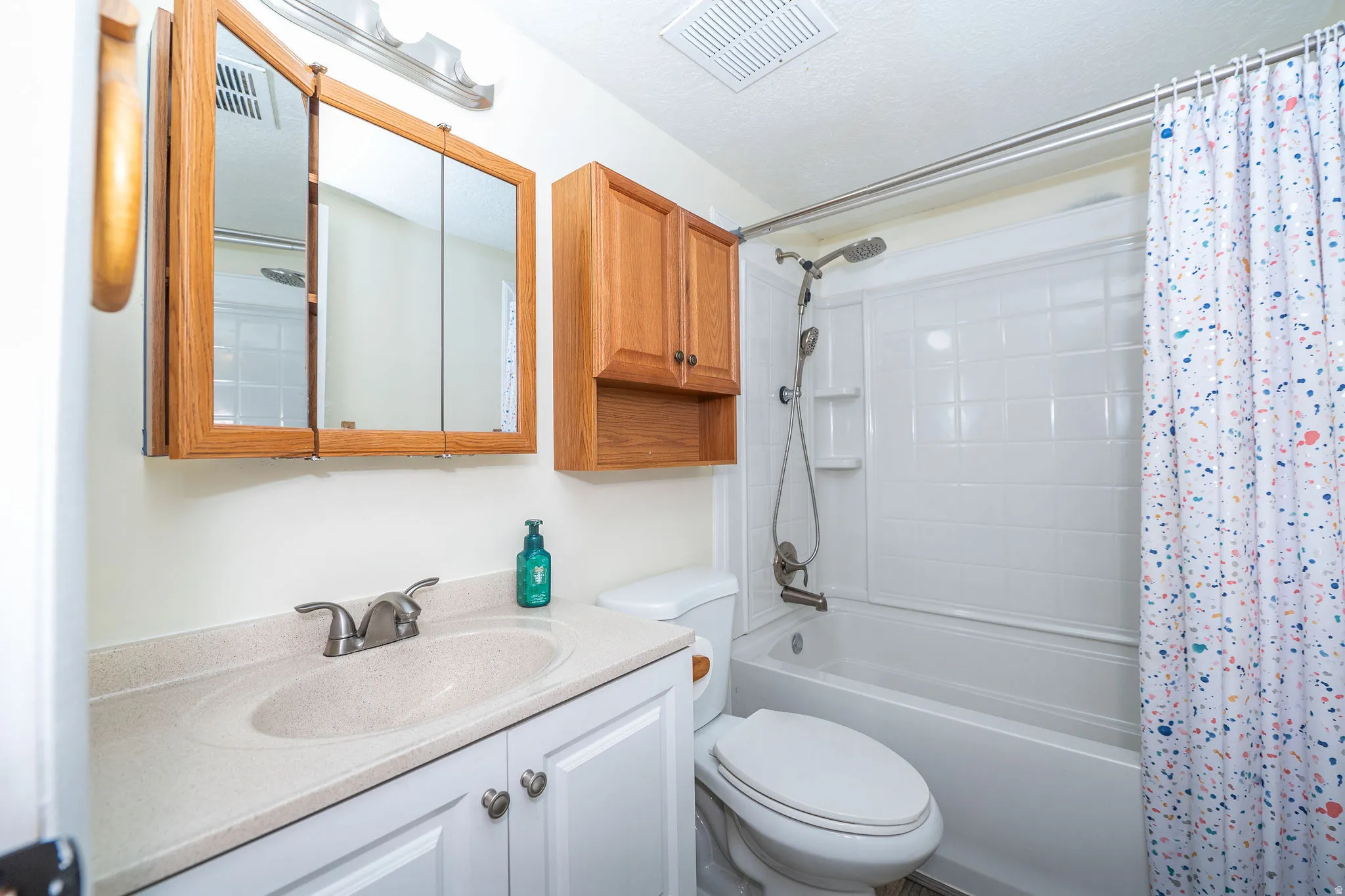 Full bathroom featuring a single vanity with an integrated sink, white cabinetry, and a mirrored medicine cabinet