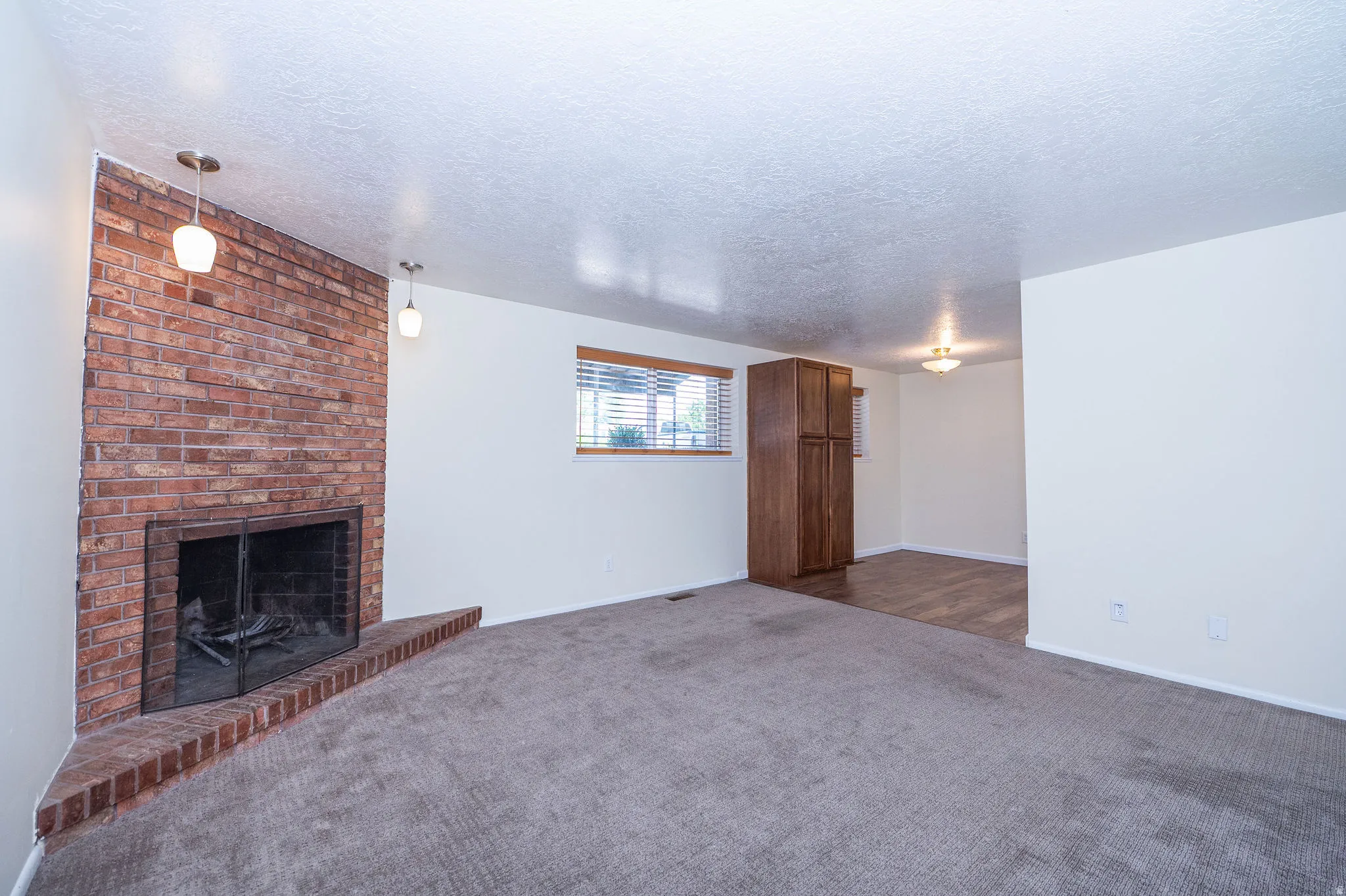 Living area featuring a brick fireplace with hearth, two pendant lights, and a window with blinds