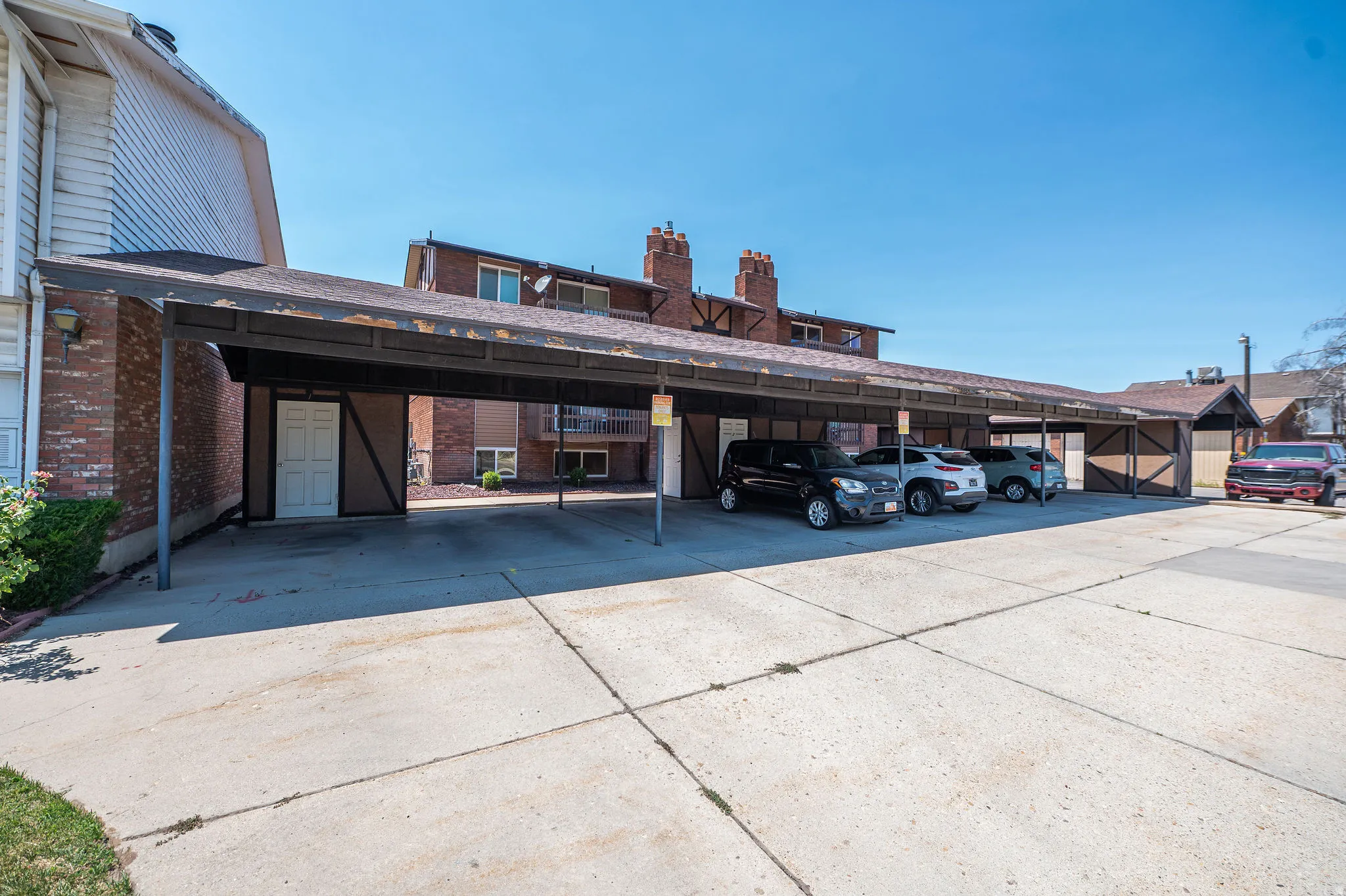 Covered parking structure with multiple spaces, featuring a sloped roof and supporting metal posts