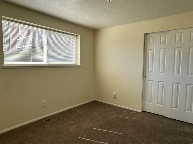 Unfurnished bedroom with dark colored carpet, a textured ceiling, and a closet
