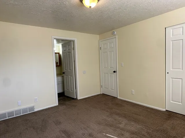 Unfurnished bedroom featuring dark carpet, a textured ceiling, and connected bathroom