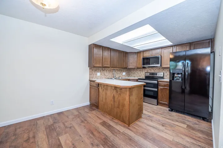 Kitchen featuring wood-finish flooring, a central island with a light-toned countertop, wood cabinetry, stainless steel appliances, and a skylight