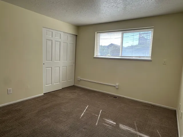 Unfurnished bedroom featuring dark carpet, a textured ceiling, and a closet