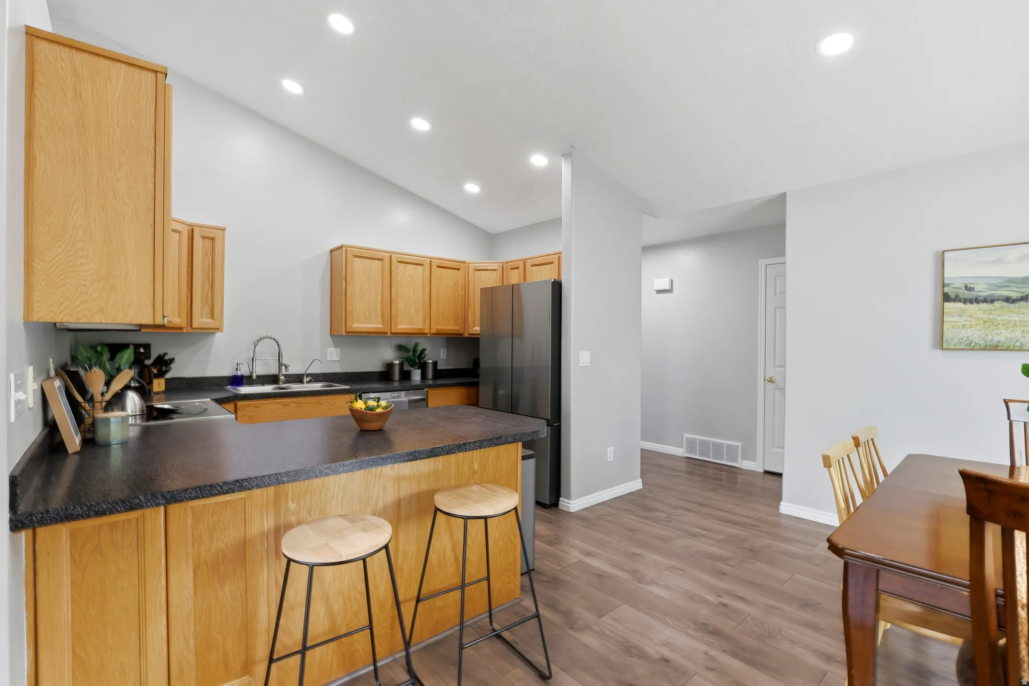 Kitchen featuring a peninsula, freestanding refrigerator, a breakfast bar area, dark countertops, and light wood-style flooring