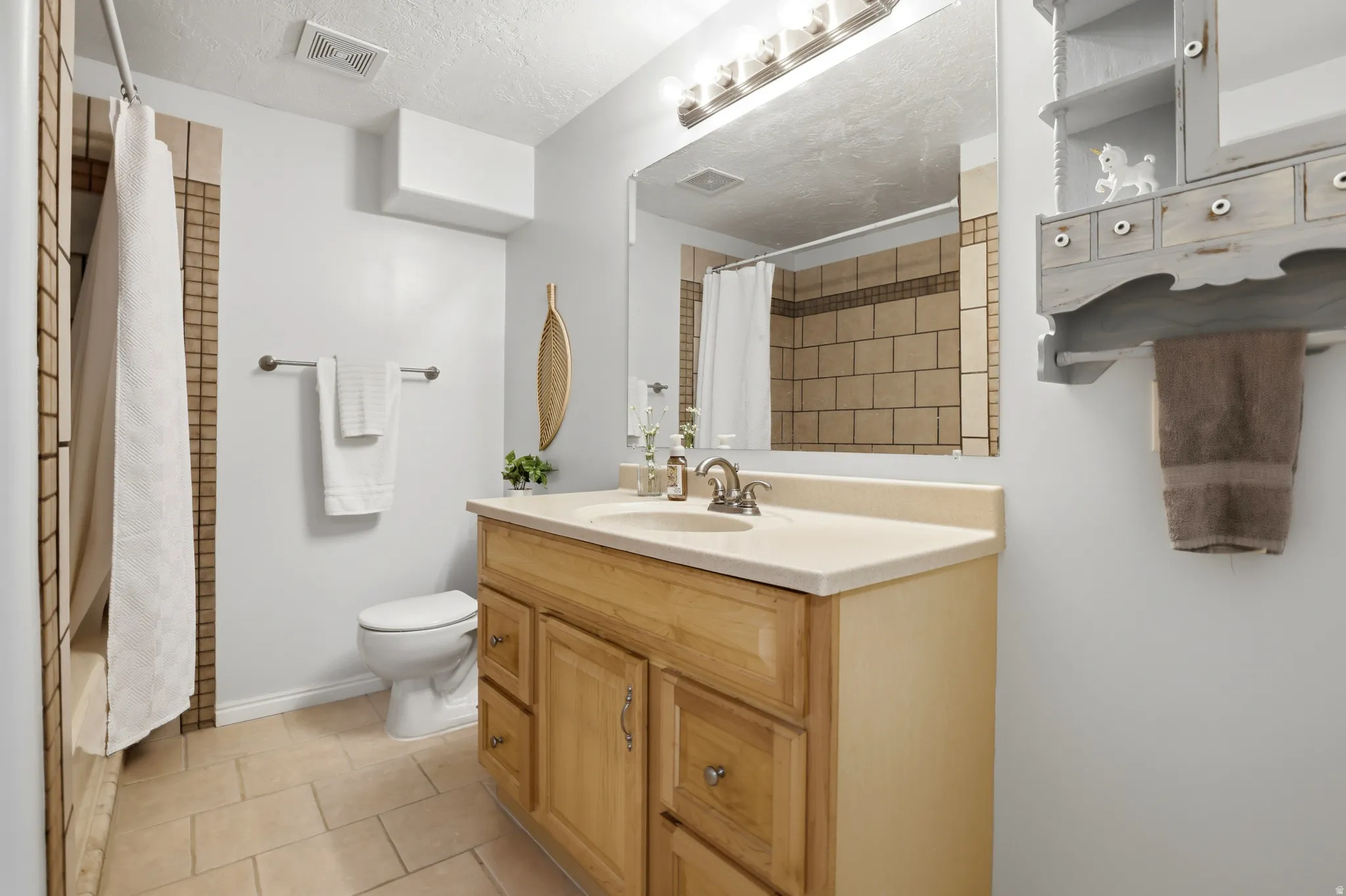 Full bath with vanity, light tile patterned floors, a textured ceiling, and shower / bath combination with curtain