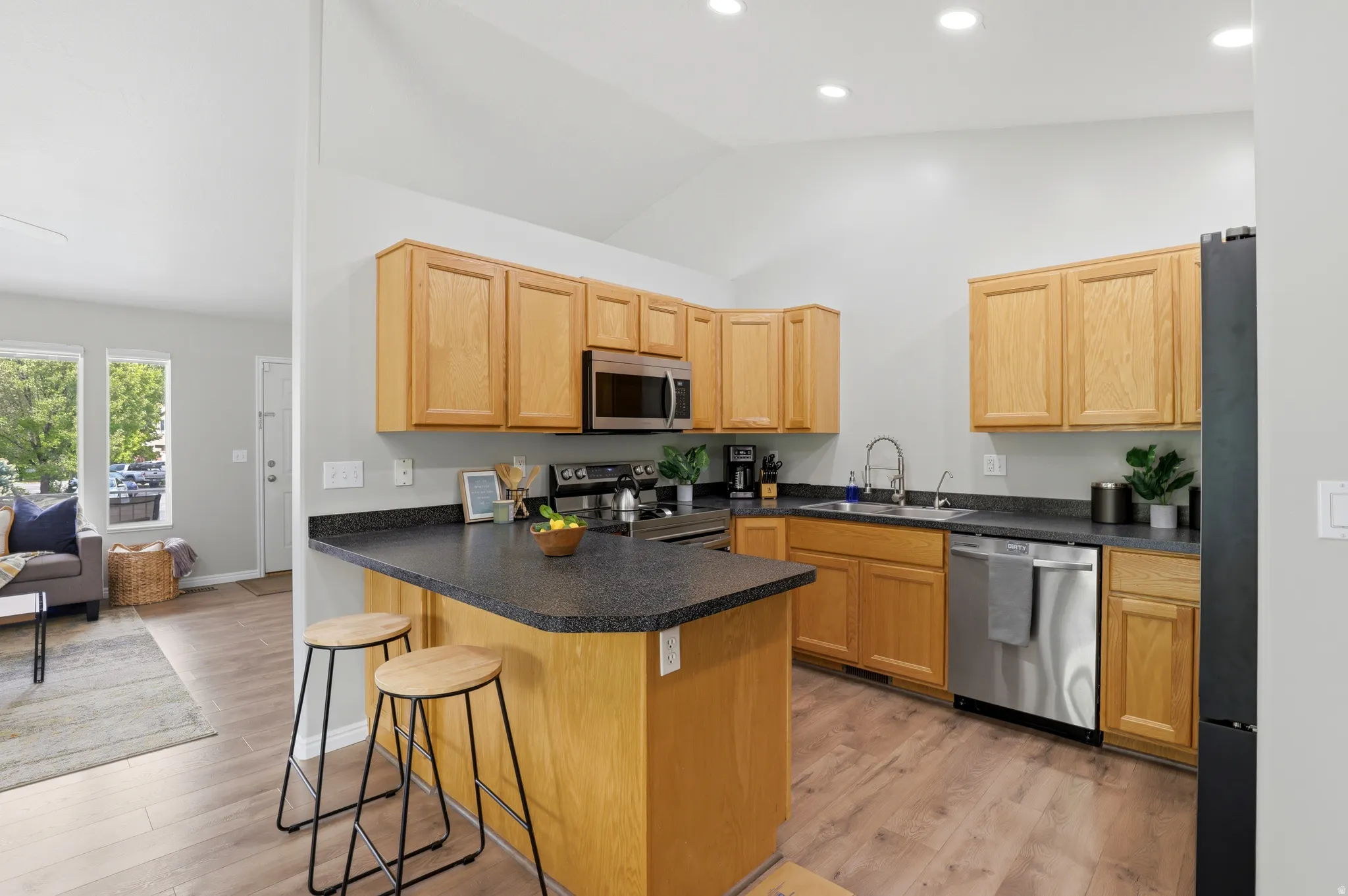 Kitchen featuring a peninsula, a breakfast bar, dark countertops, light wood finished floors, and lofted ceiling